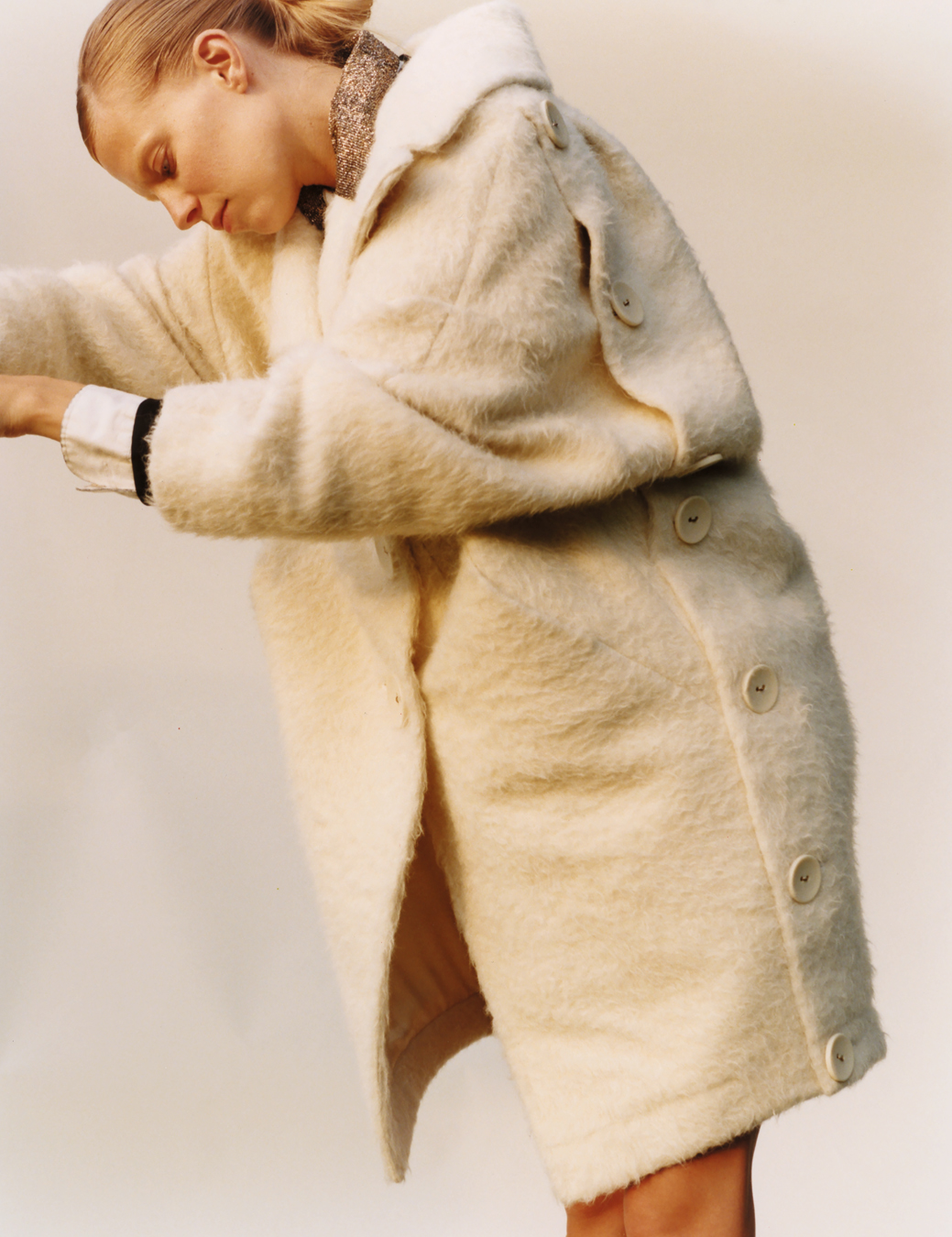 a woman wears a creme fluffy coat with large buttons down the side