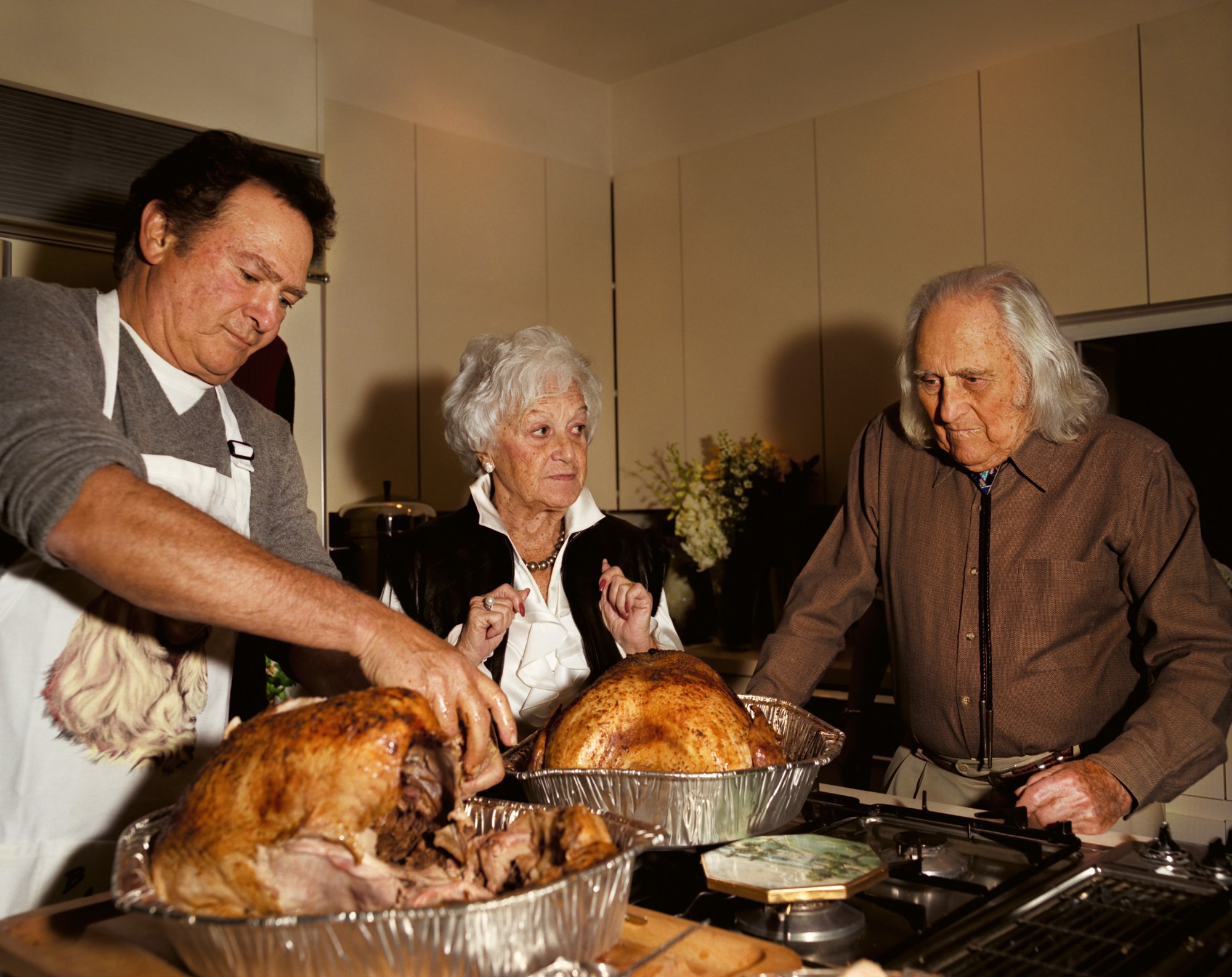 a man carves a turkey while an older man and woman stand by another turkey