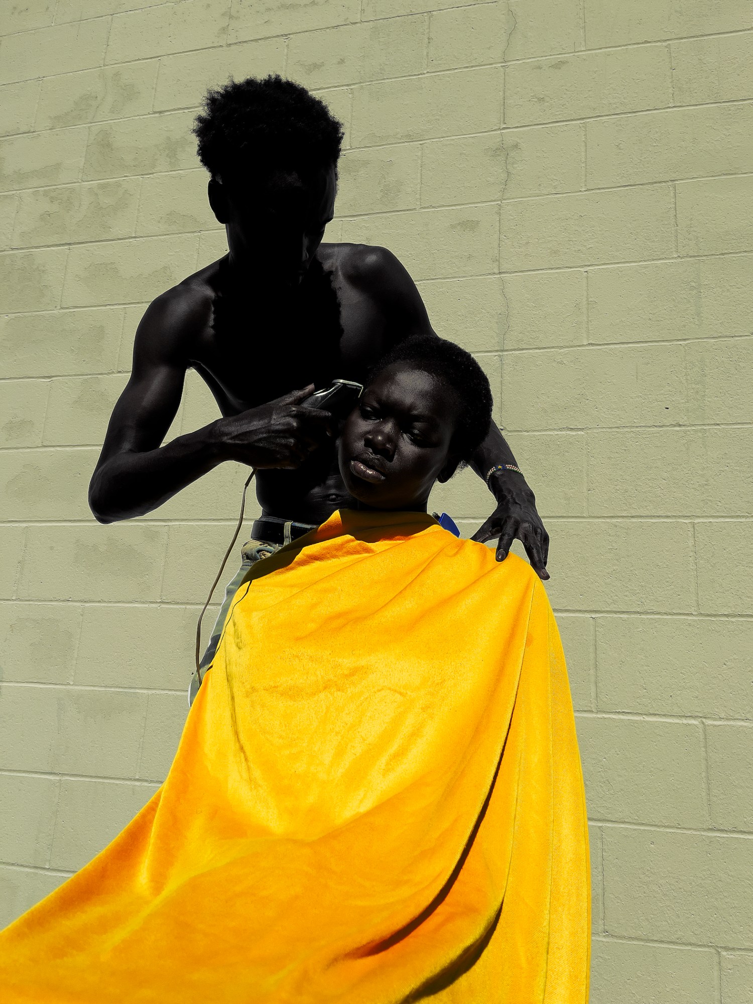 a boy giving another a hair cut in a bright yellow smock by isaac west