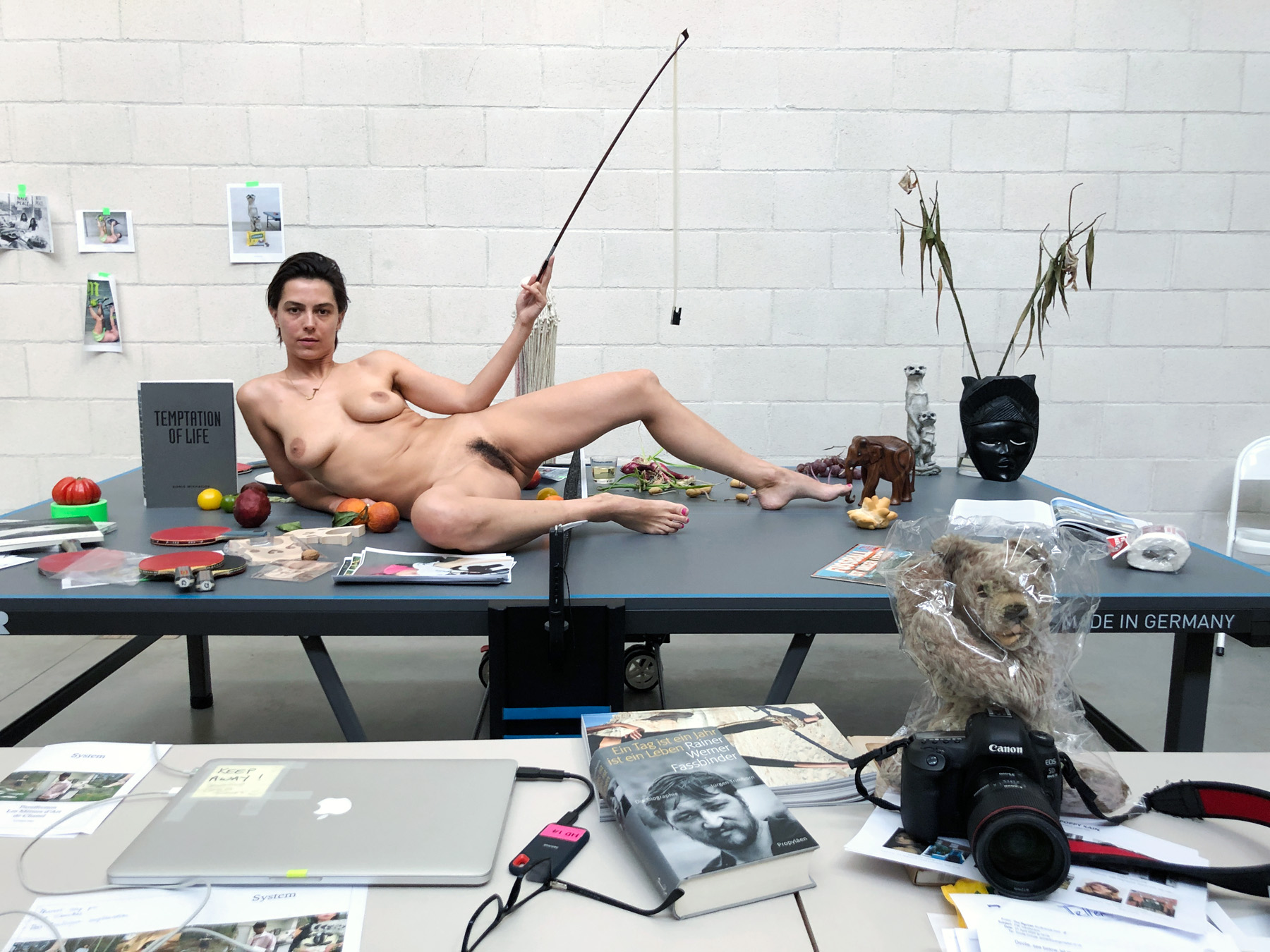 a woman lies naked on a ping pong table surrounded by miscellaneous objects