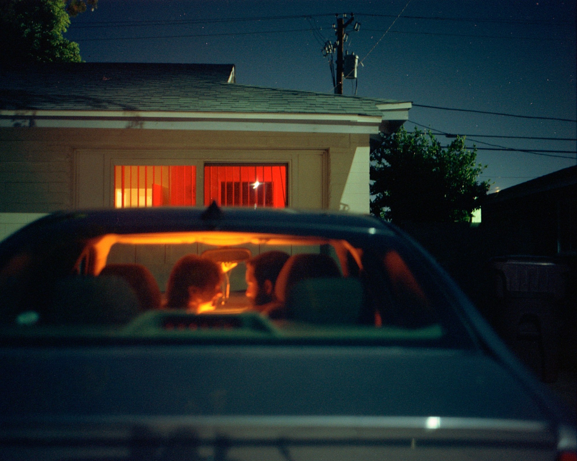 A couple sit in the front seats of a car parked in front of a house staring into each others eyes.