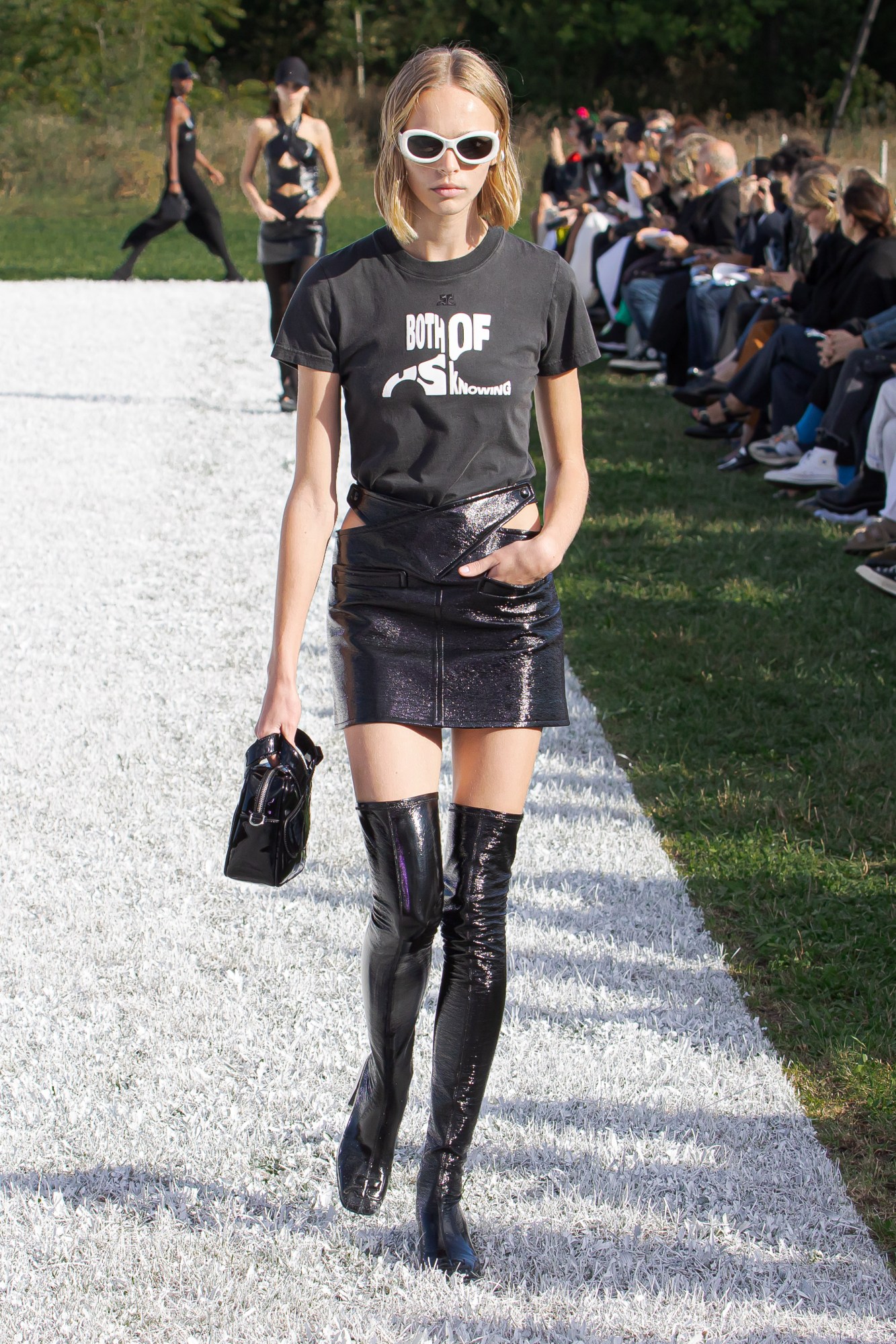 Courreges SS22 catwalk look: a model wears thigh-high black boots with a PVC mini skirt and a band-style tee