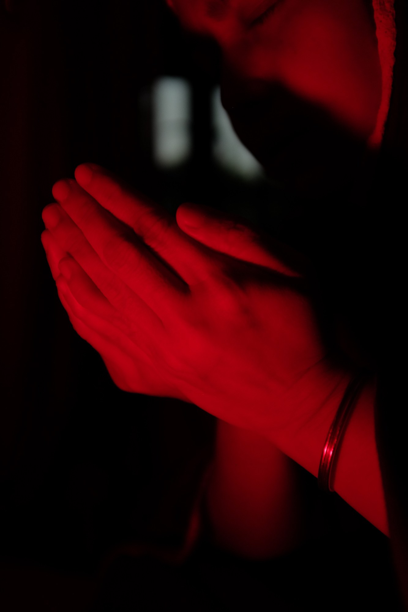 Hands together in prayer under a red light