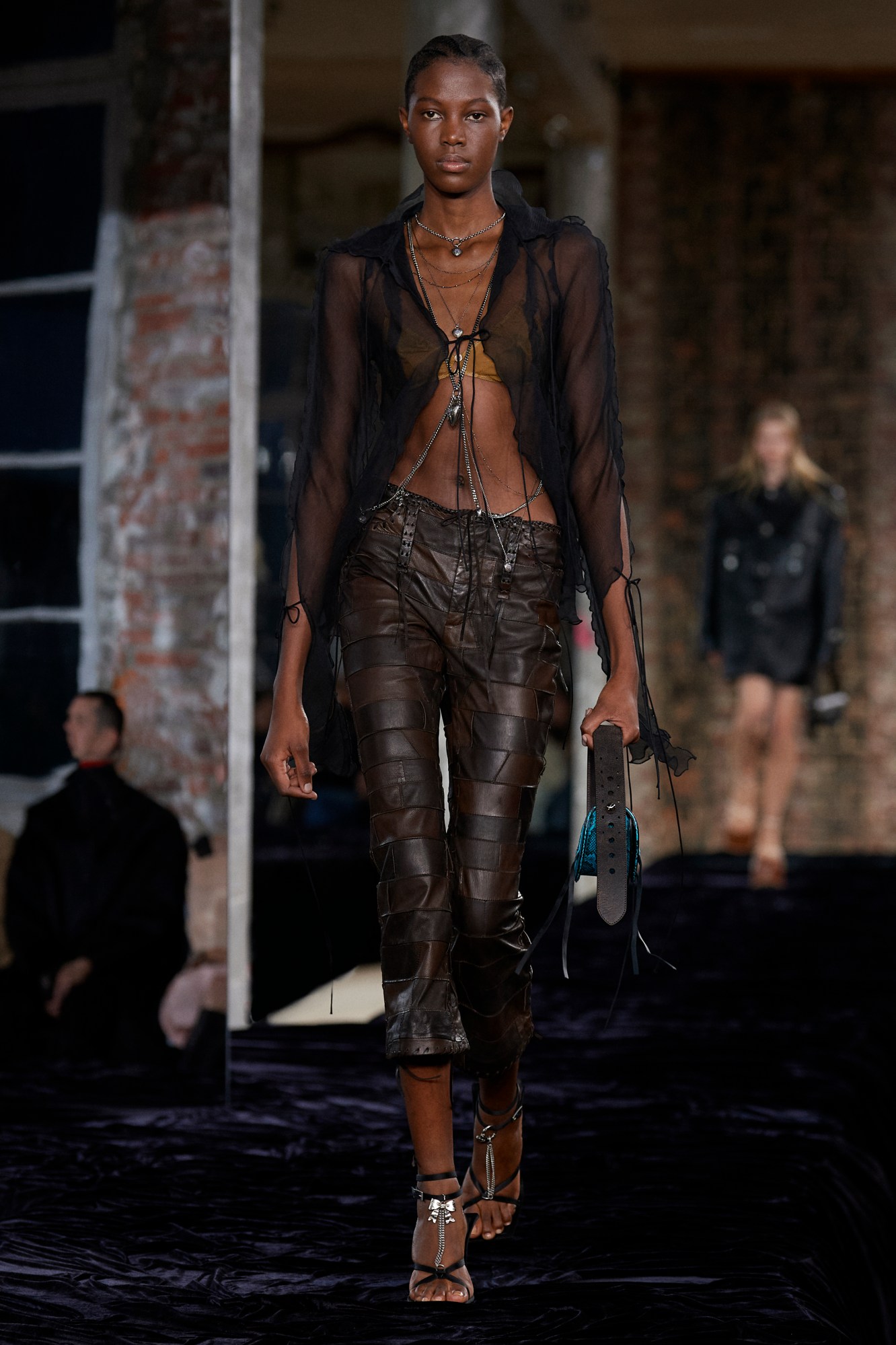 Acne Studios SS22: a model wears patchwork brown leather trousers with a sheer black floaty top