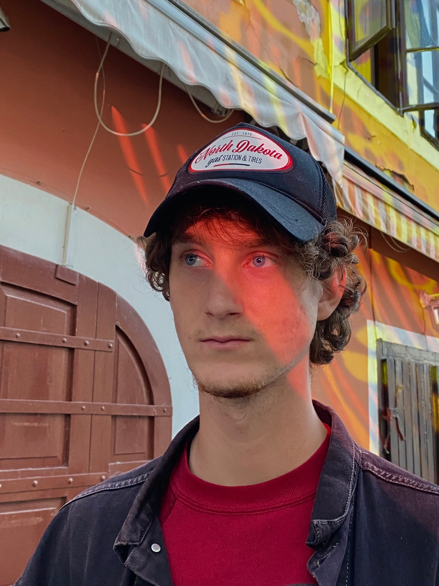 Portrait of a man outside a door. The light reflects on their face.