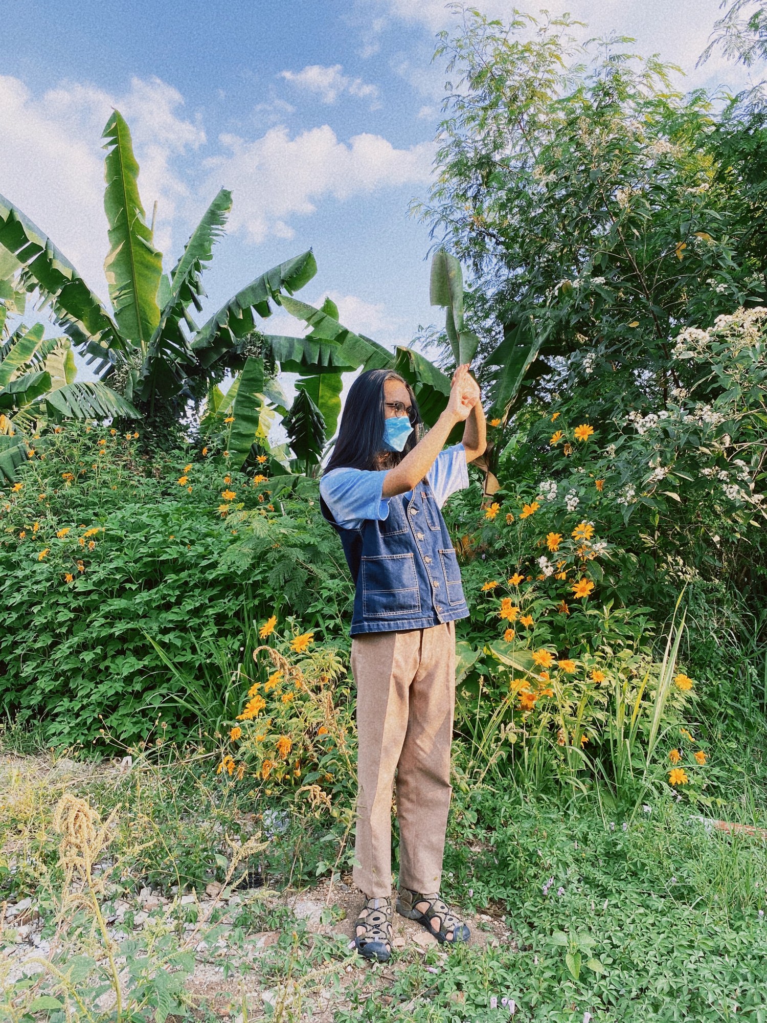 Person standing amongst grass, bushes and trees.