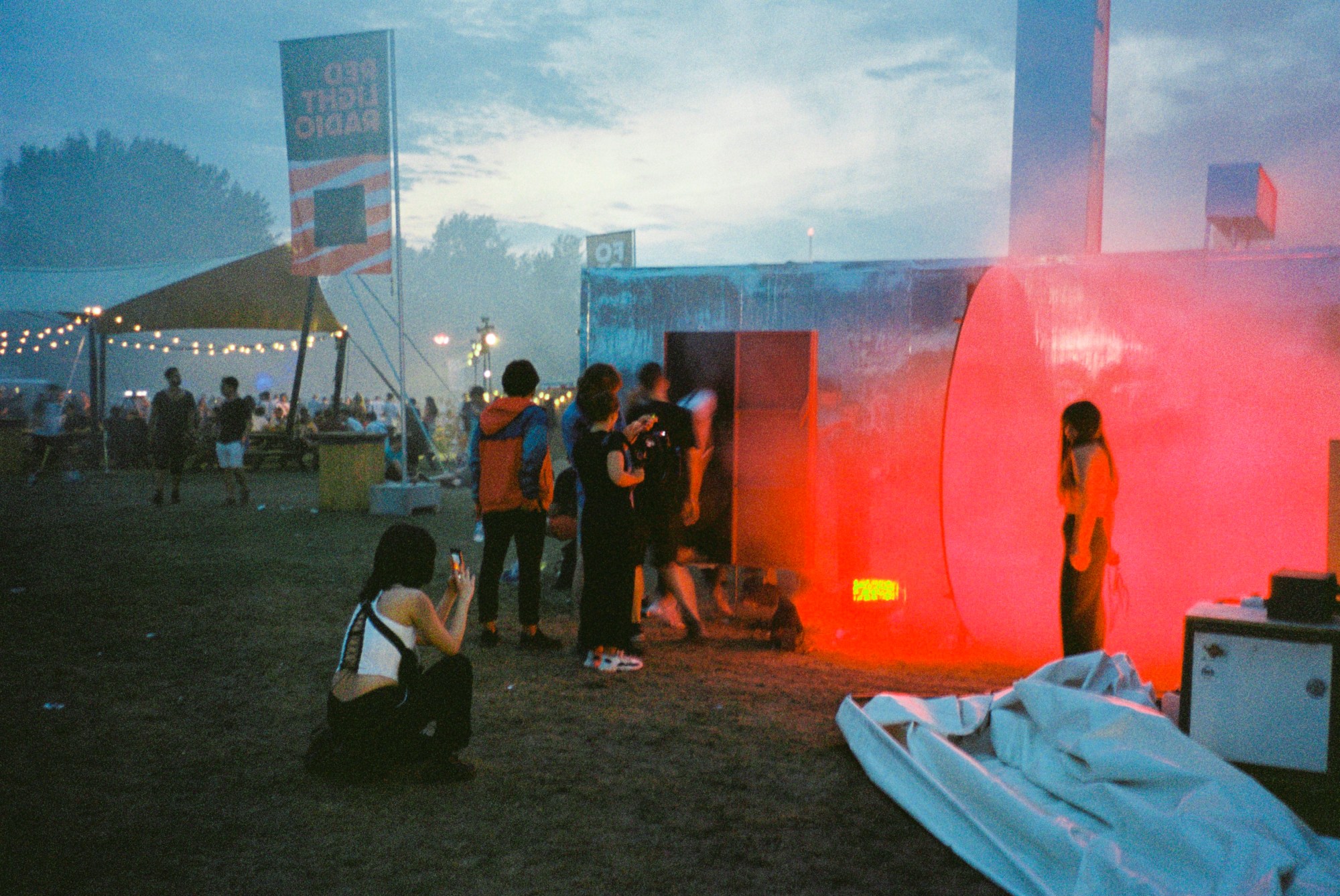 a festival scene in which somebody takes a photograph of their friend standing in some neon red-lit mist