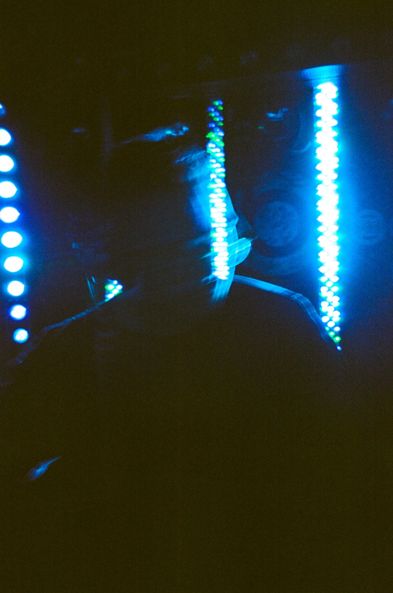 a blurred figure in glasses stands in front of blue neon lights