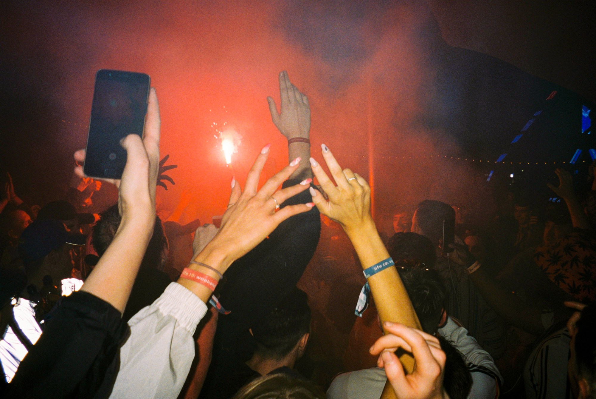 hands are raised to the sky in a red smokey festival crowd scene