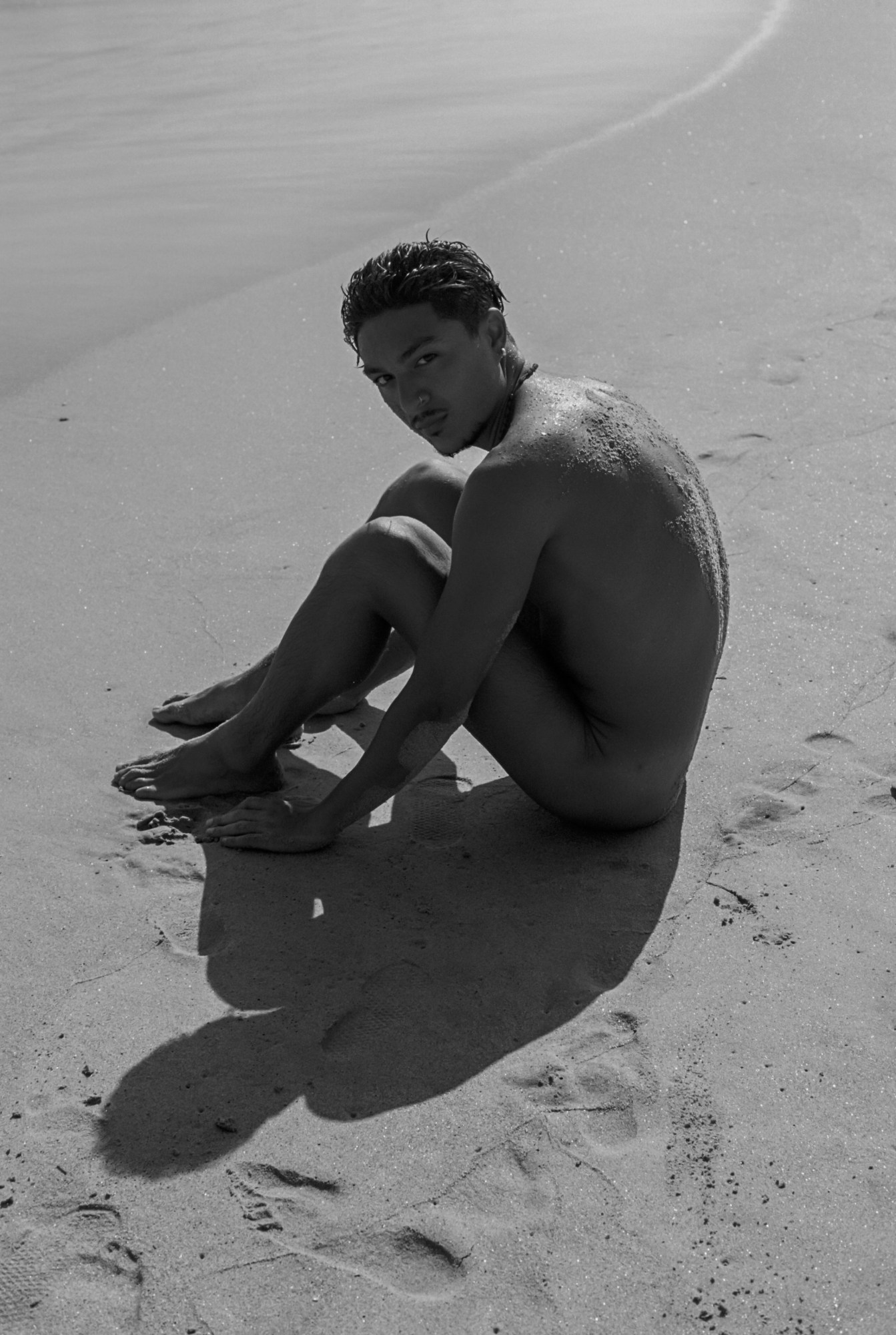 a man sits naked on the beach in sand