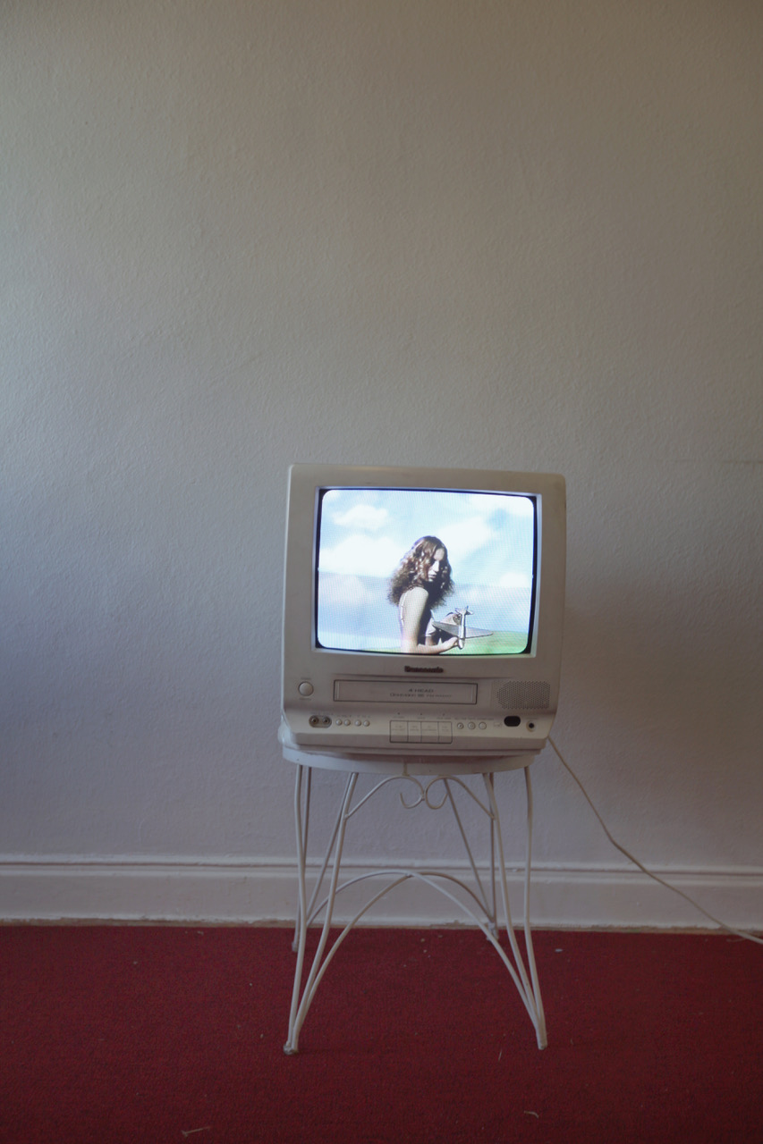 an old fashioned tv resting on a stool in front of a white wall and red carpet