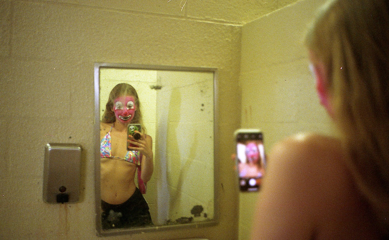 a woman in clown makeup takes a selfie in a dirty mirror