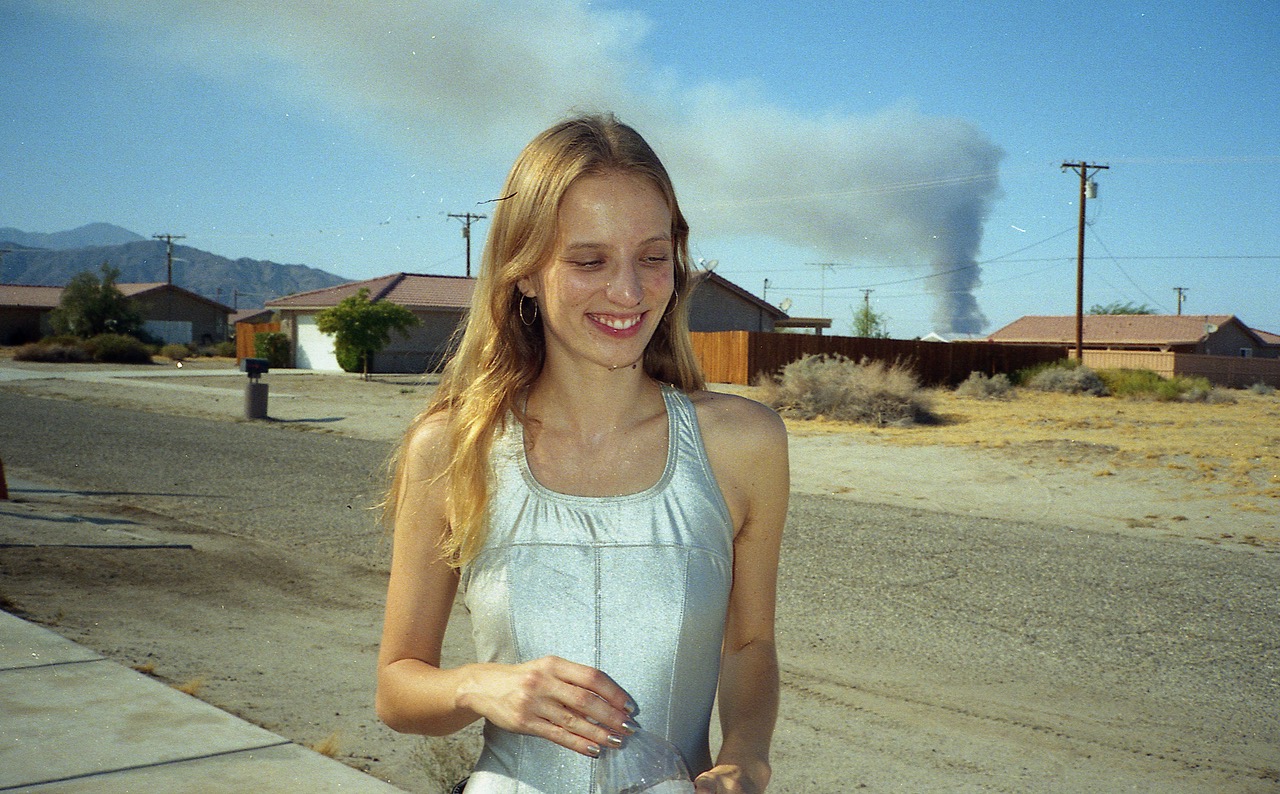 a woman in a silver swimsuit stands and smiles as smoke billows in the background