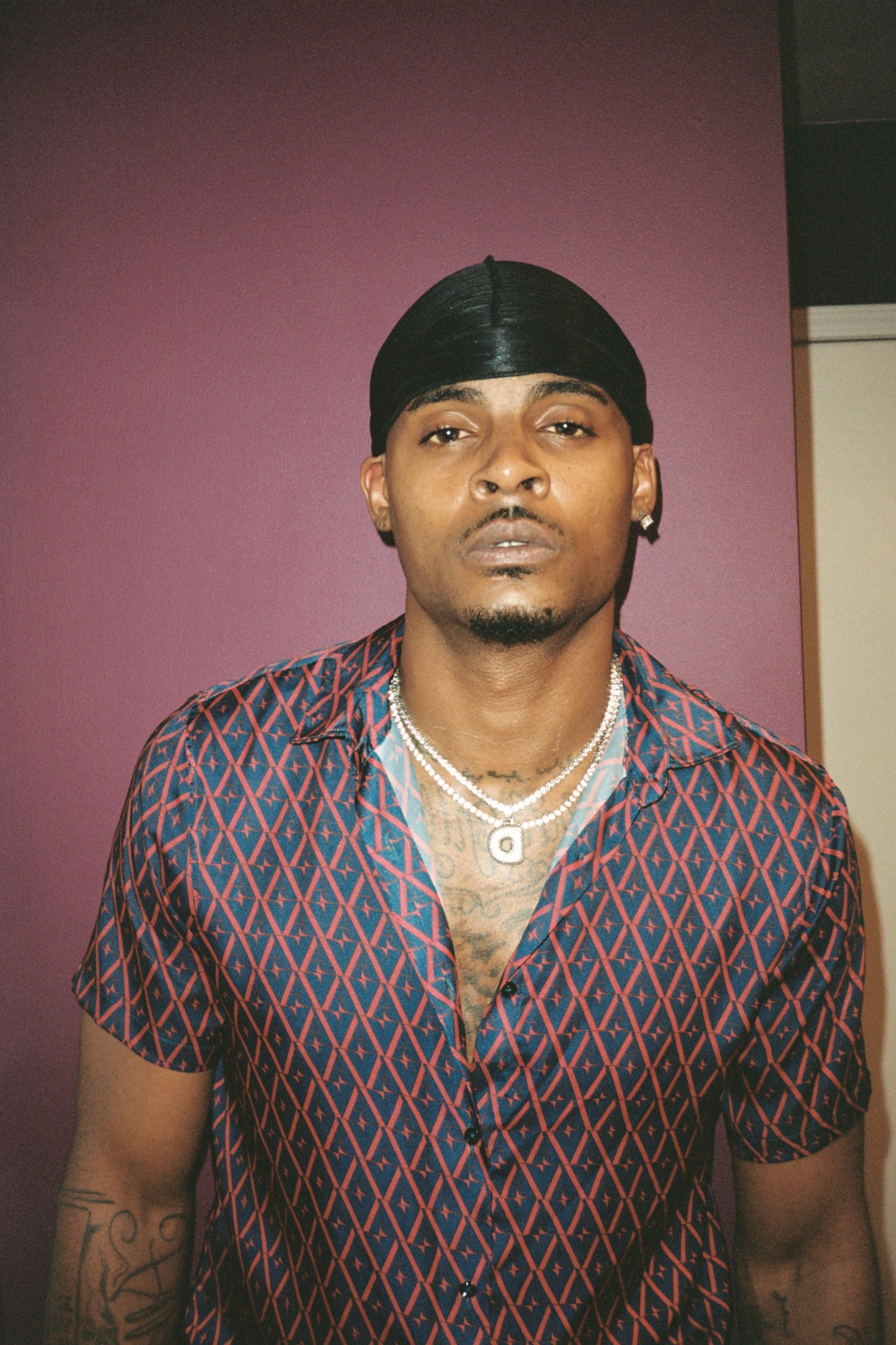 a portrait of a man in an open shirt wearing a durag and two strings of pearls