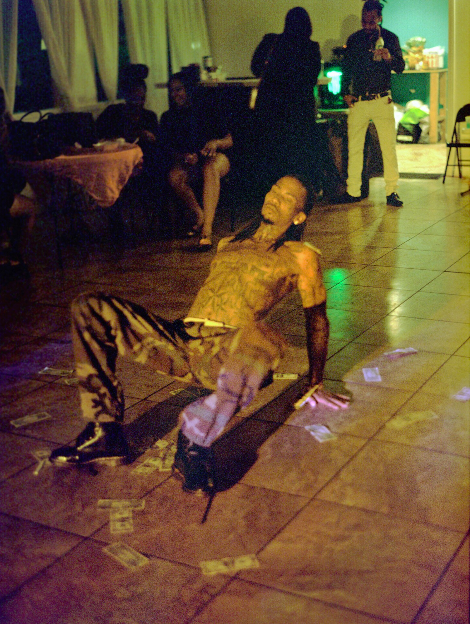 a tattooed man wearing camo dances on a floor littered with dollar bills