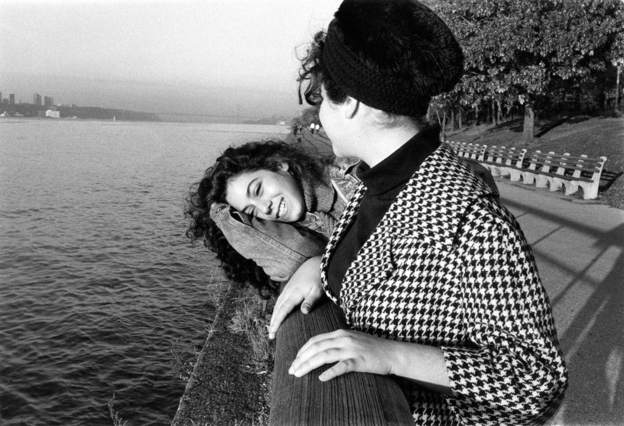 two women leaning on the wall that borders a river