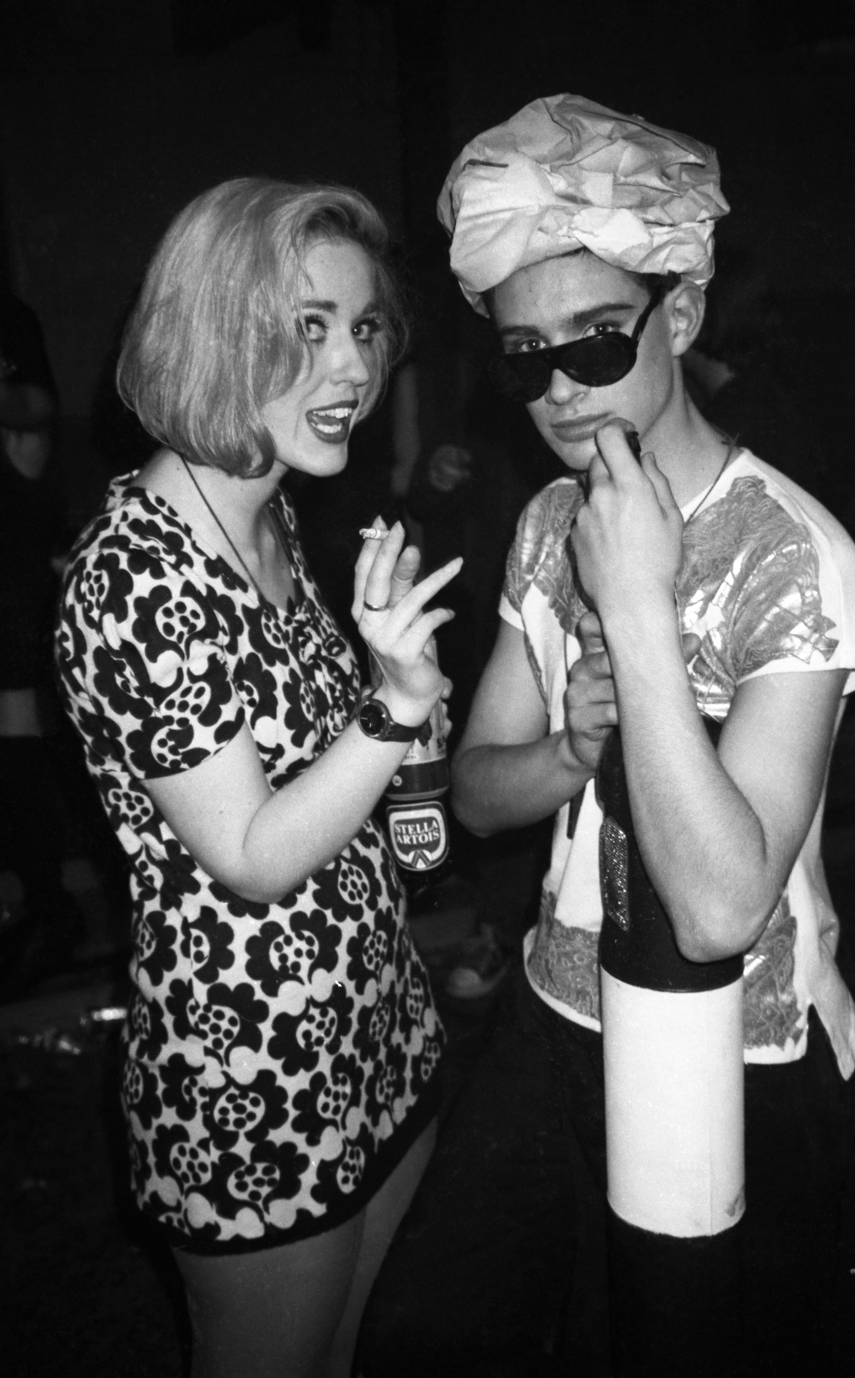 a woman smoking and drinking on the left and a man in sunglasses with a headdress on his head