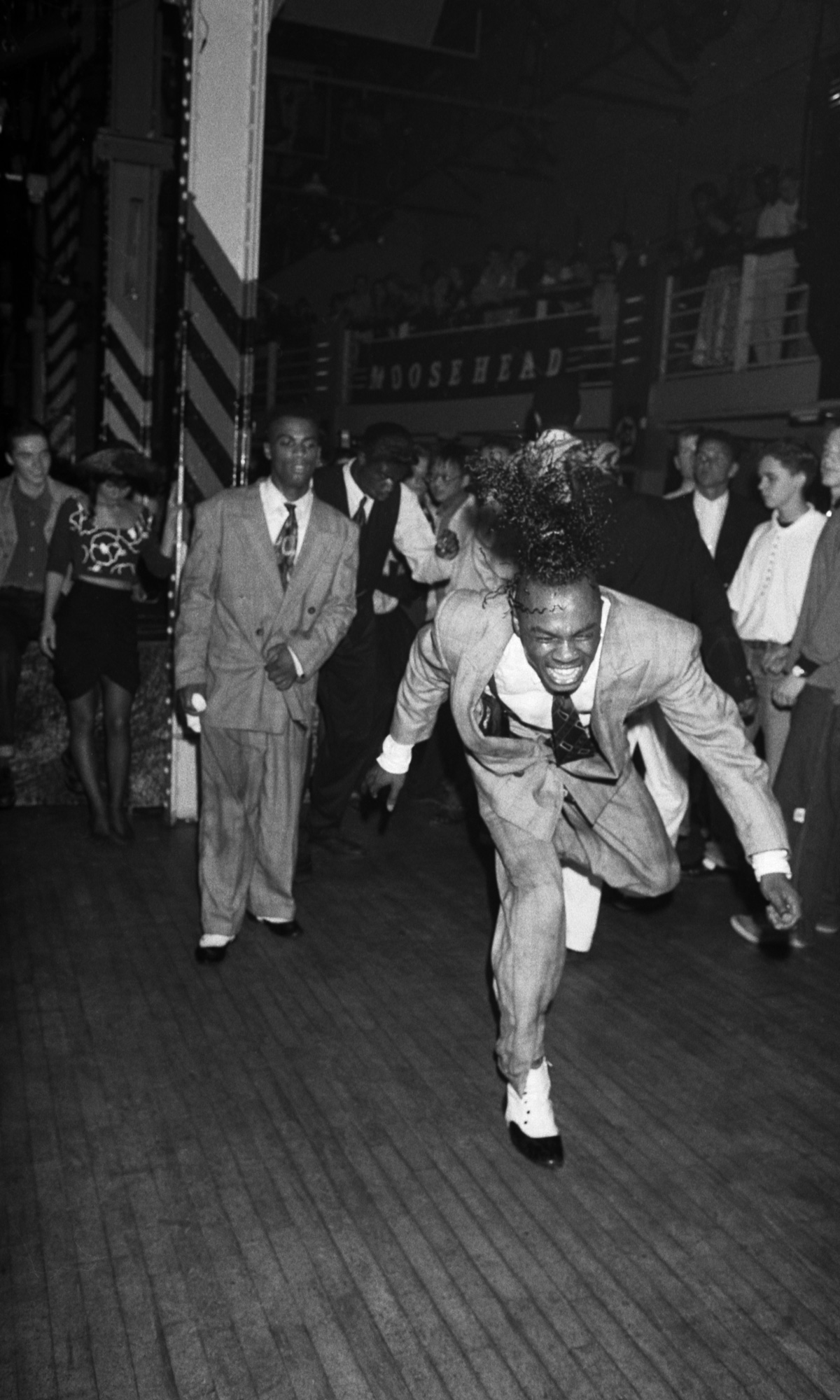 two men in suits dancing in a cleared space in a club