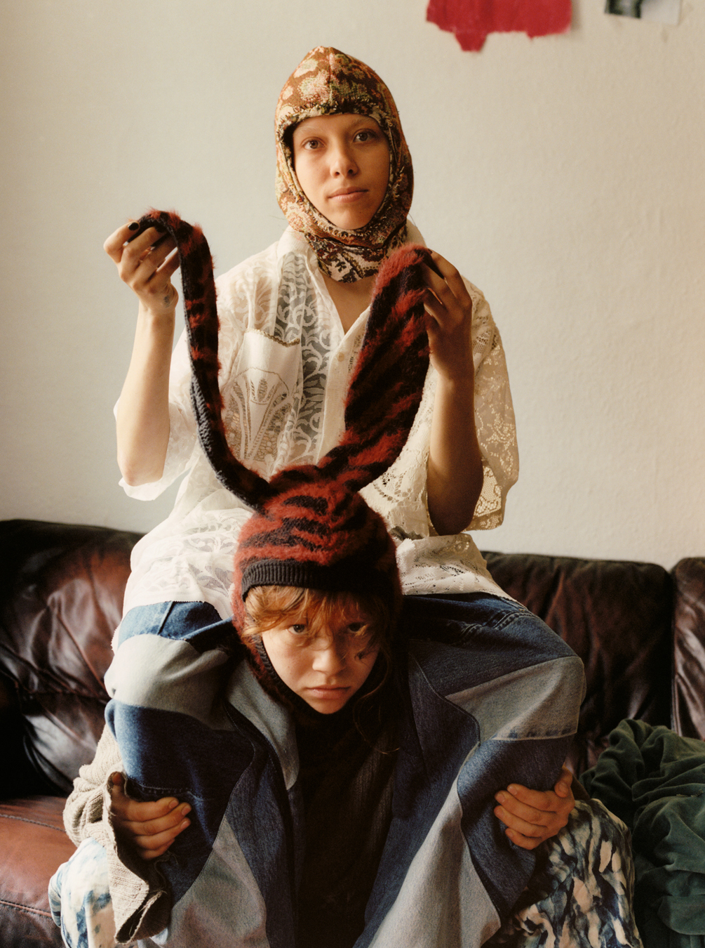 Lola + Pani photograph of a model in patchwork jeans sitting on another's shoulders, holding the ears of his rabbit-eared balaclava