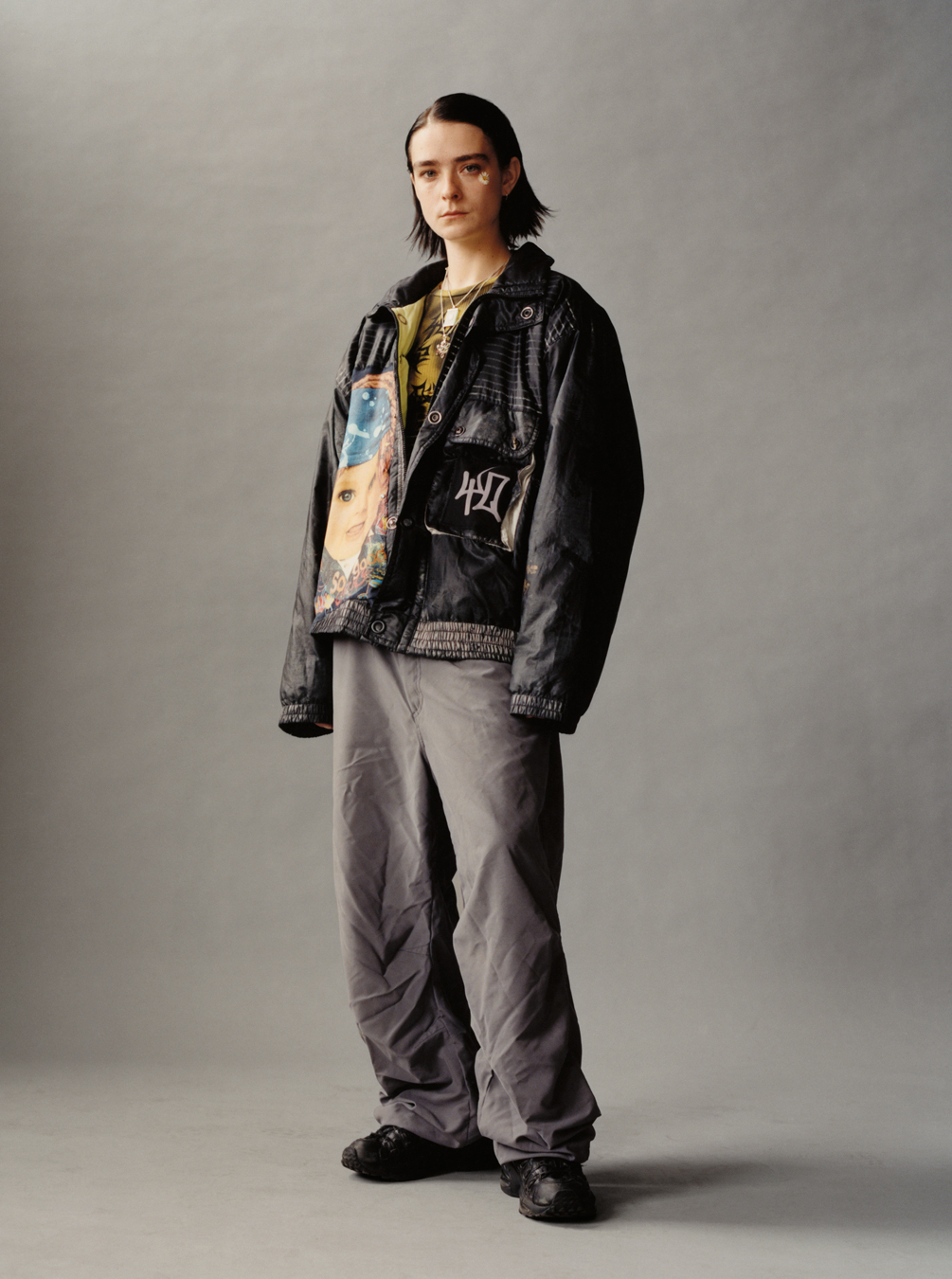 a model wears grey walking trousers and a custom oversized jacket, standing and looking to camera