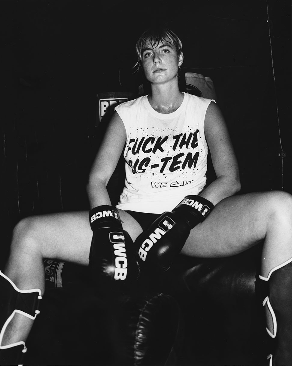 a person wearing boxing gloves and a t-shirt that reads 'fuck the cis-tem'