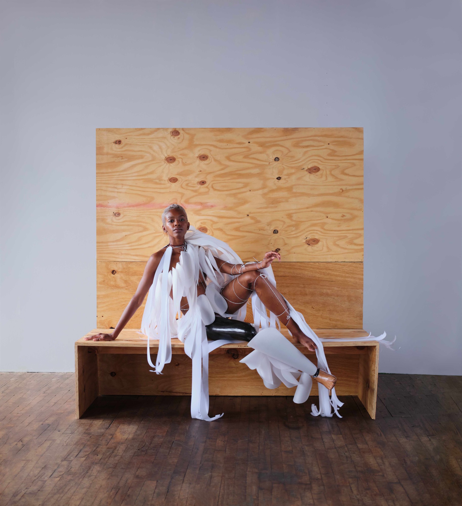 Kiara Marshal sitting on a wooden bench wearing a paper scultpure by Karina Sharif. Photo Director Paula Andrea.