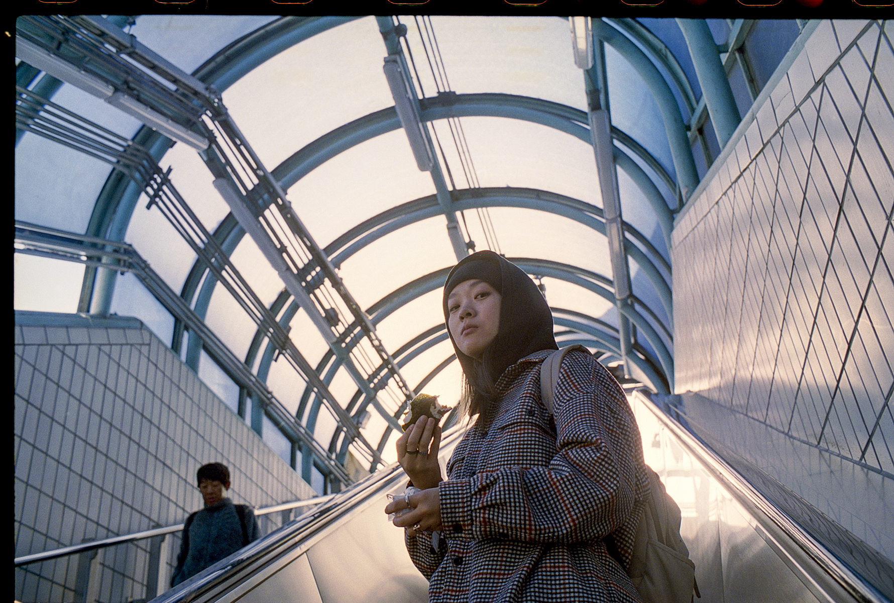 a woman eats something whilst stood on an escalator