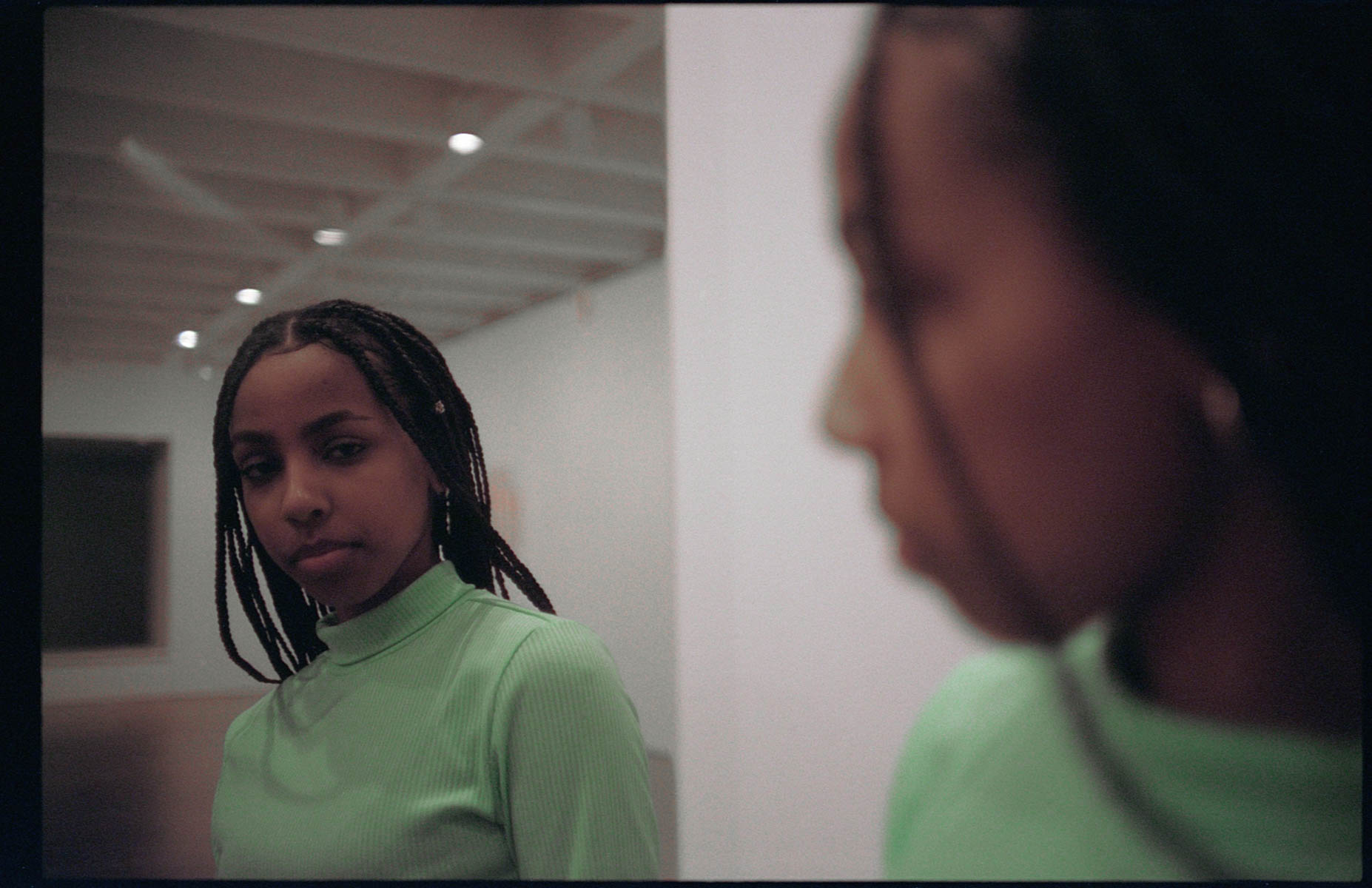 a young woman looks at her own reflection in an empty gallery space