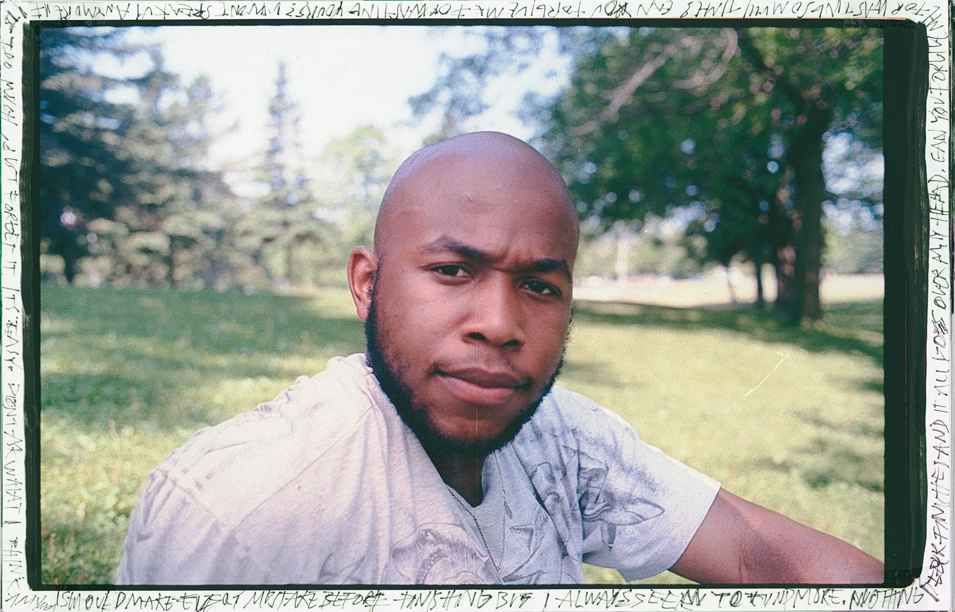 a young man looks into the camera, sat in a park