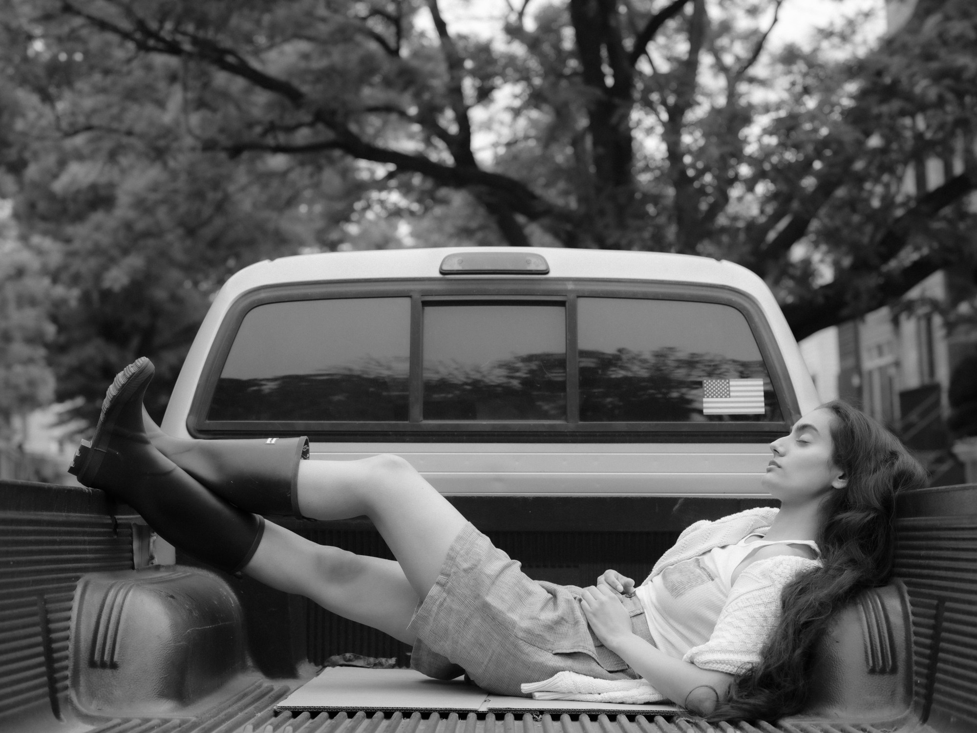 A girl in wellies lounges on the back of a pick up truck