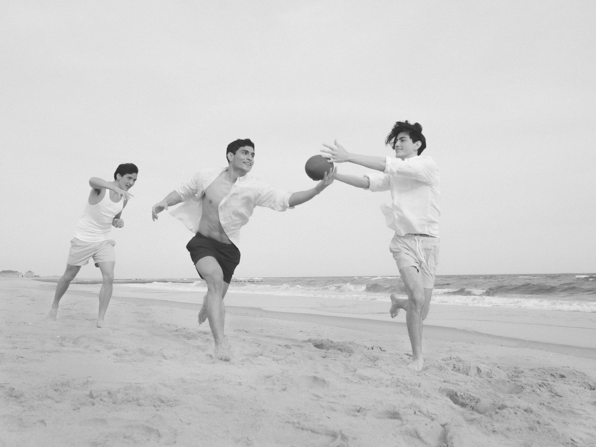 three boys play american football on the beach.