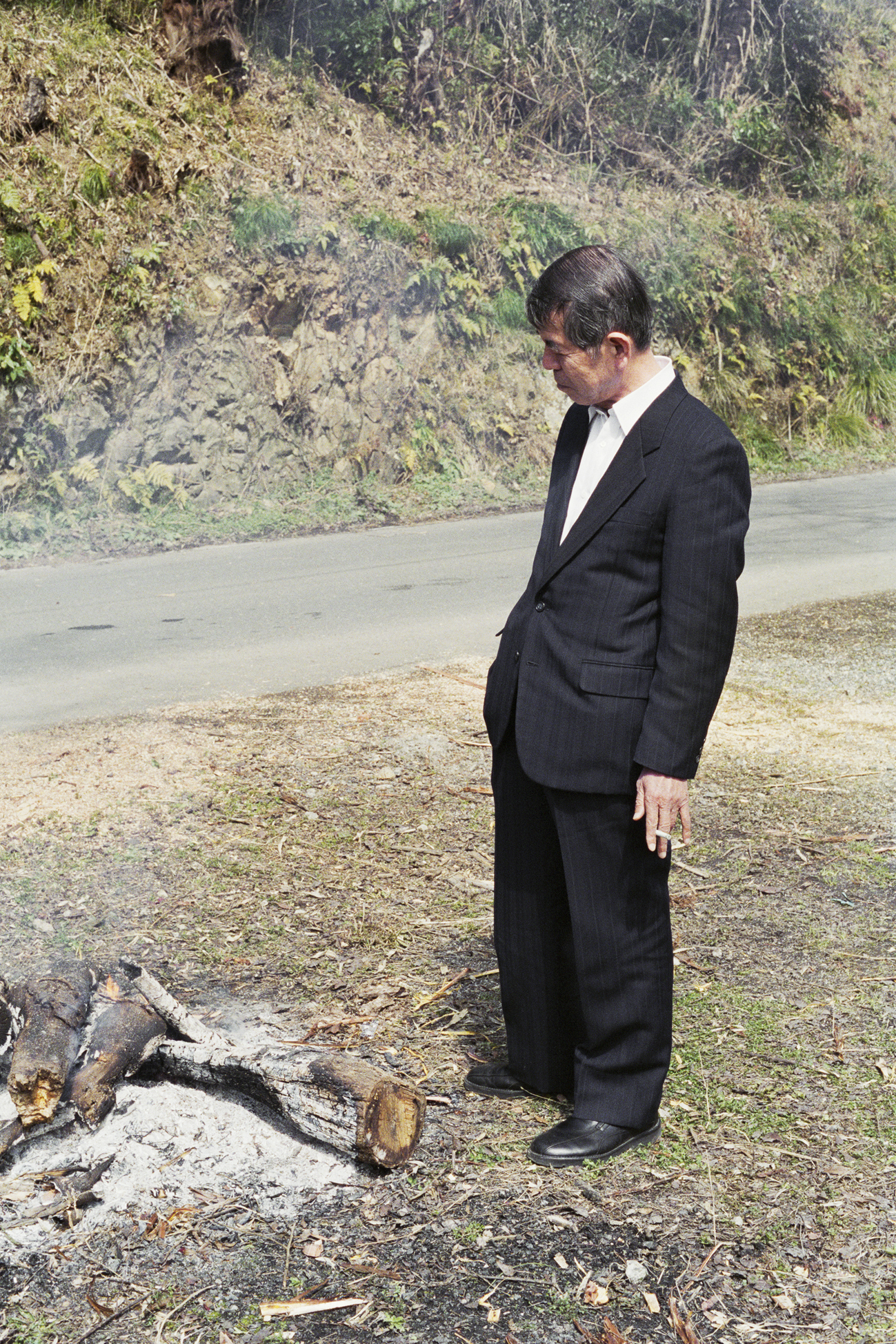 an older man in a suit stood next to some burnt logs