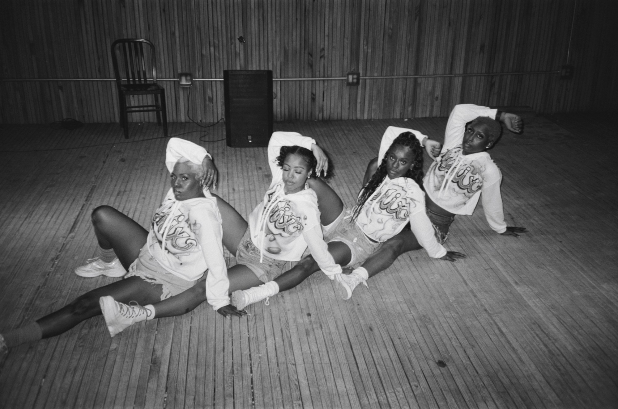 Four women wearing white hooded sweatshirts posing on the floor.