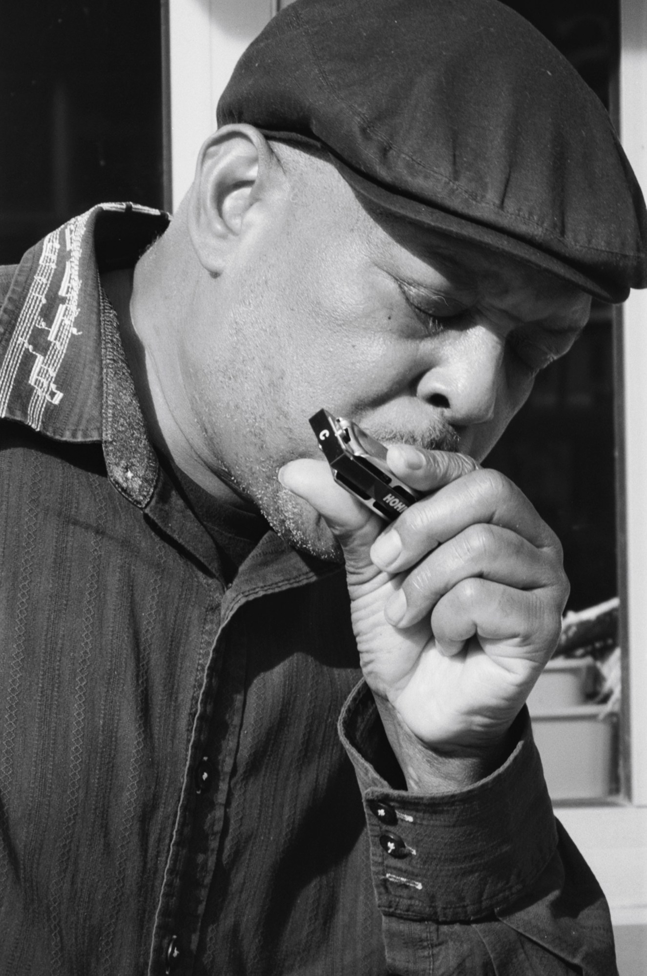 A portrait of a man wearing a flat cap playing a harmonica