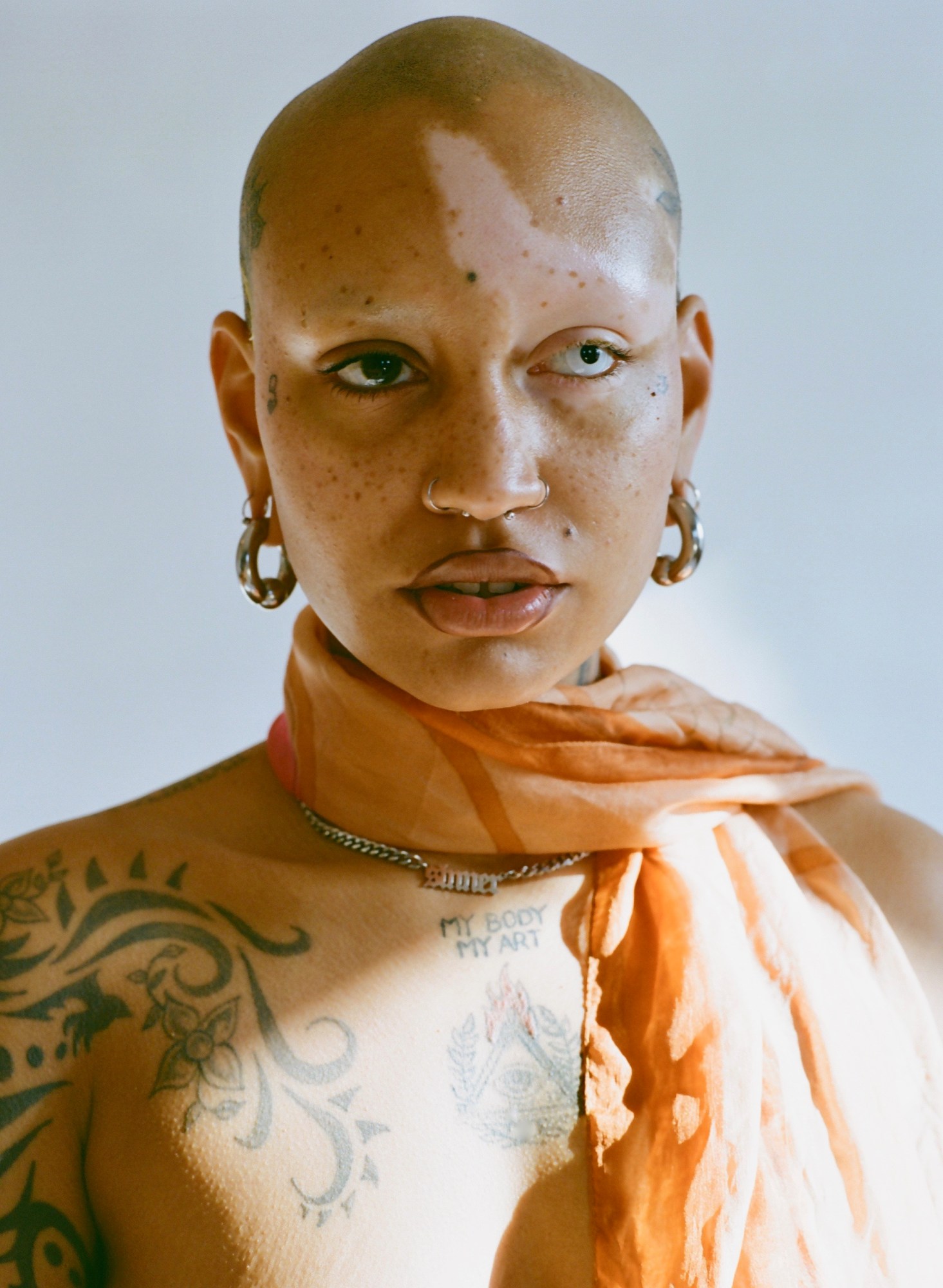 Portrait of a model with tattoos on body, an orange scarf and chain necklace.