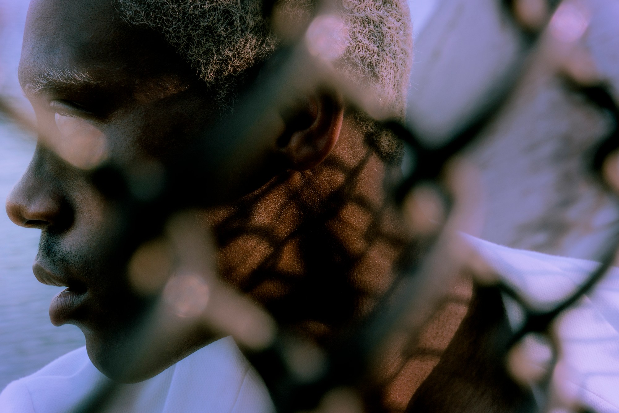 side profile of man behind a hatched wire fence.