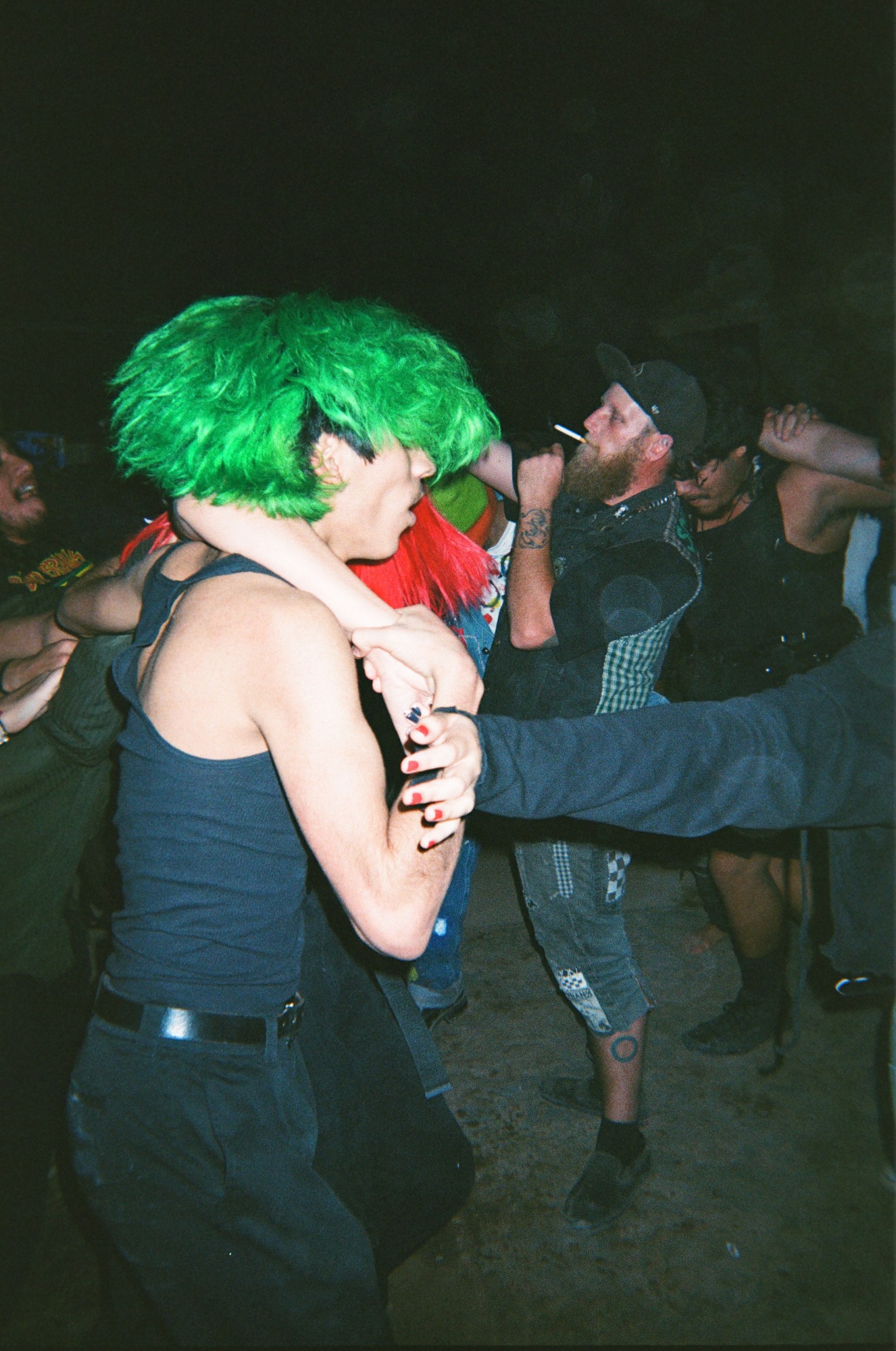 Person with green hair holds up someone else as they make their way through a crowd.