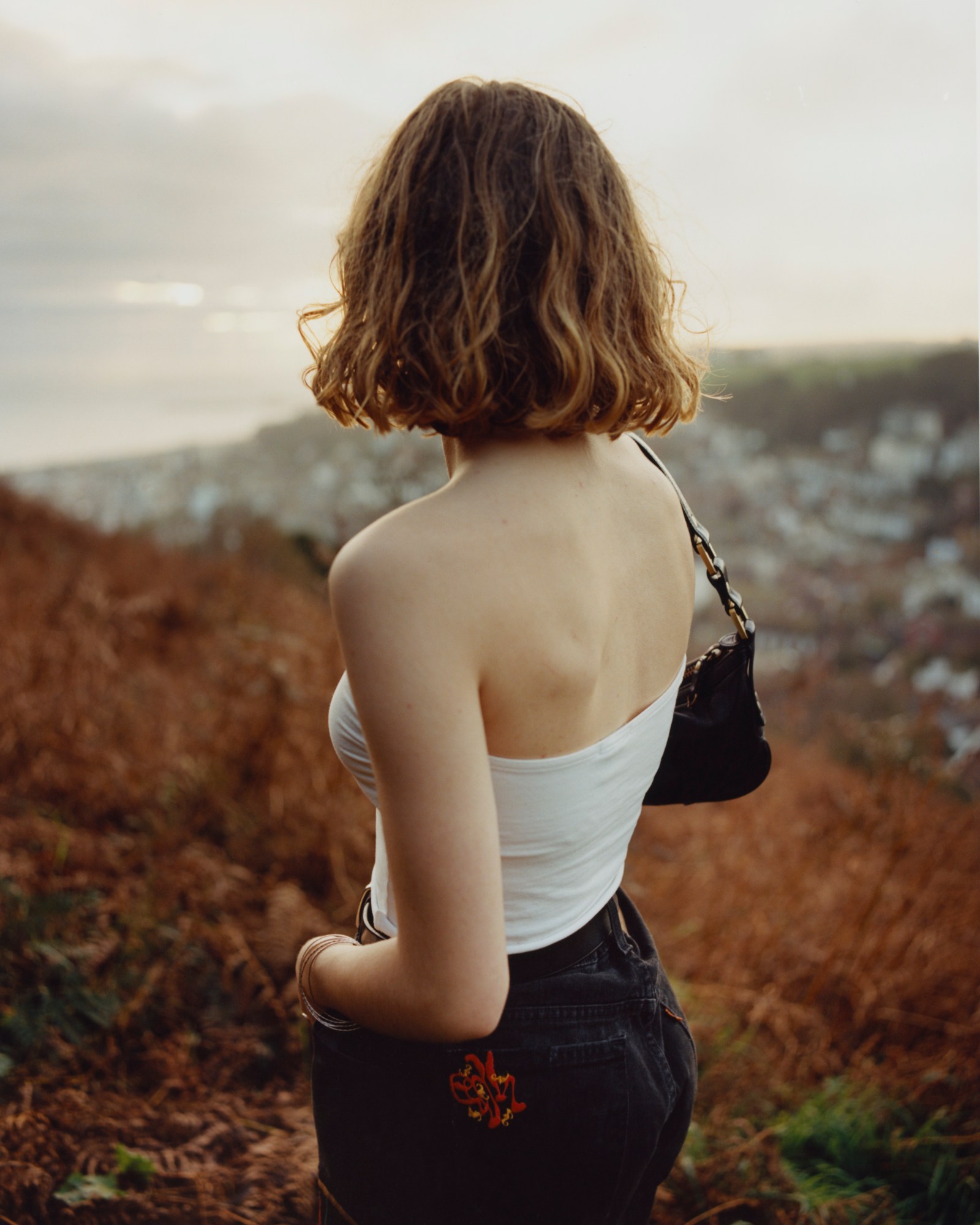 Girl in embroidered jeans and white top looks out over town.