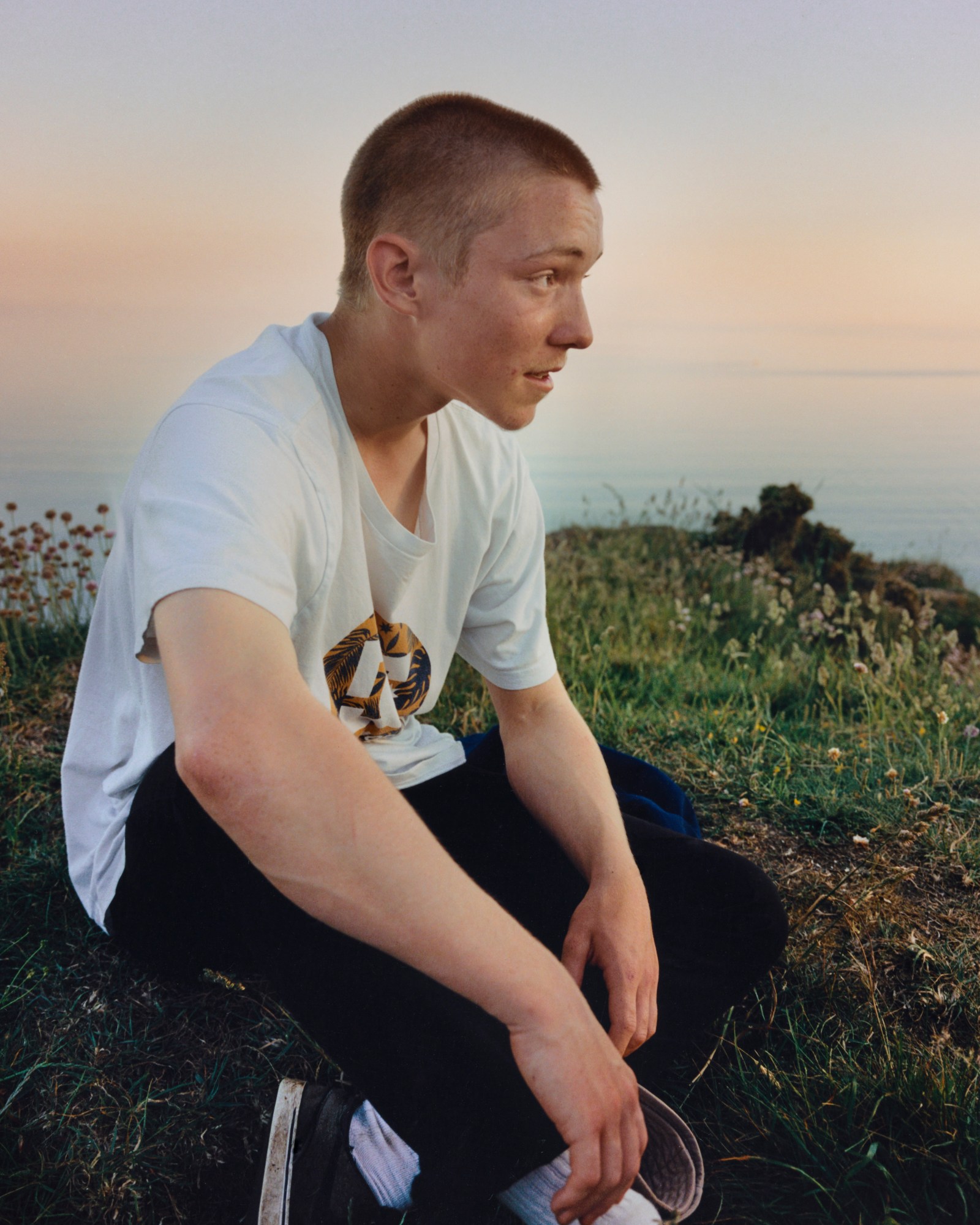 boy in white tee sitting cross legged on grass