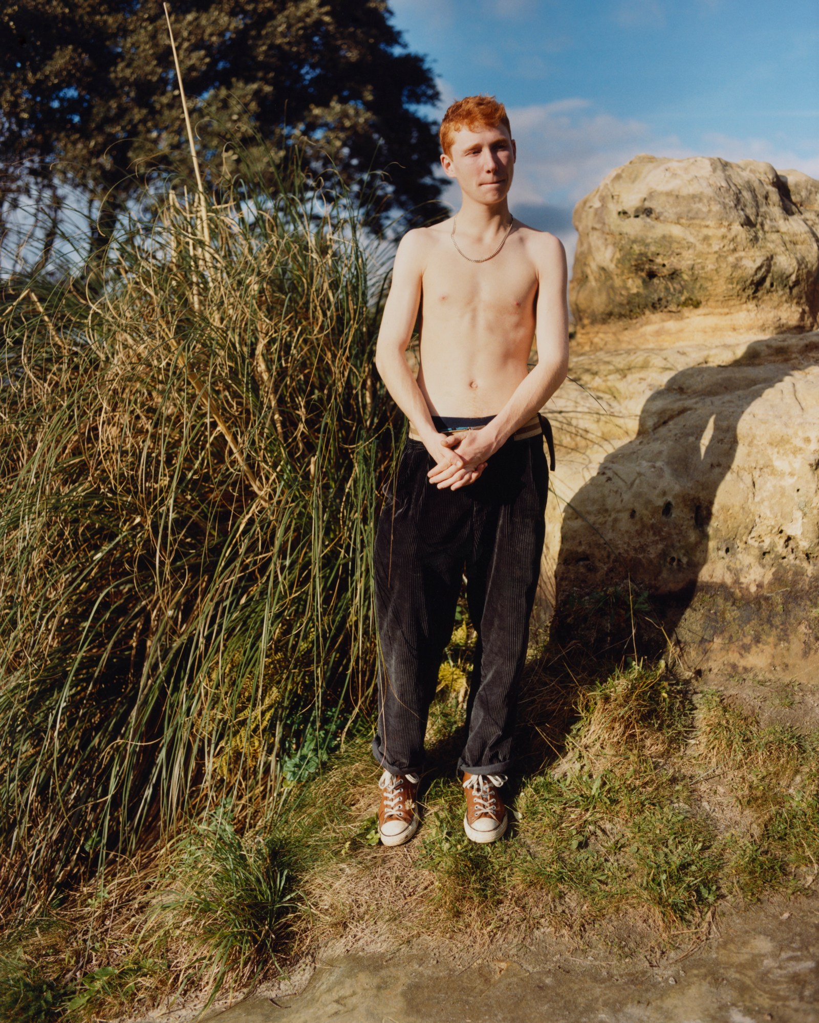 boy in jeans and shirtless standing amongst rocks and bushes