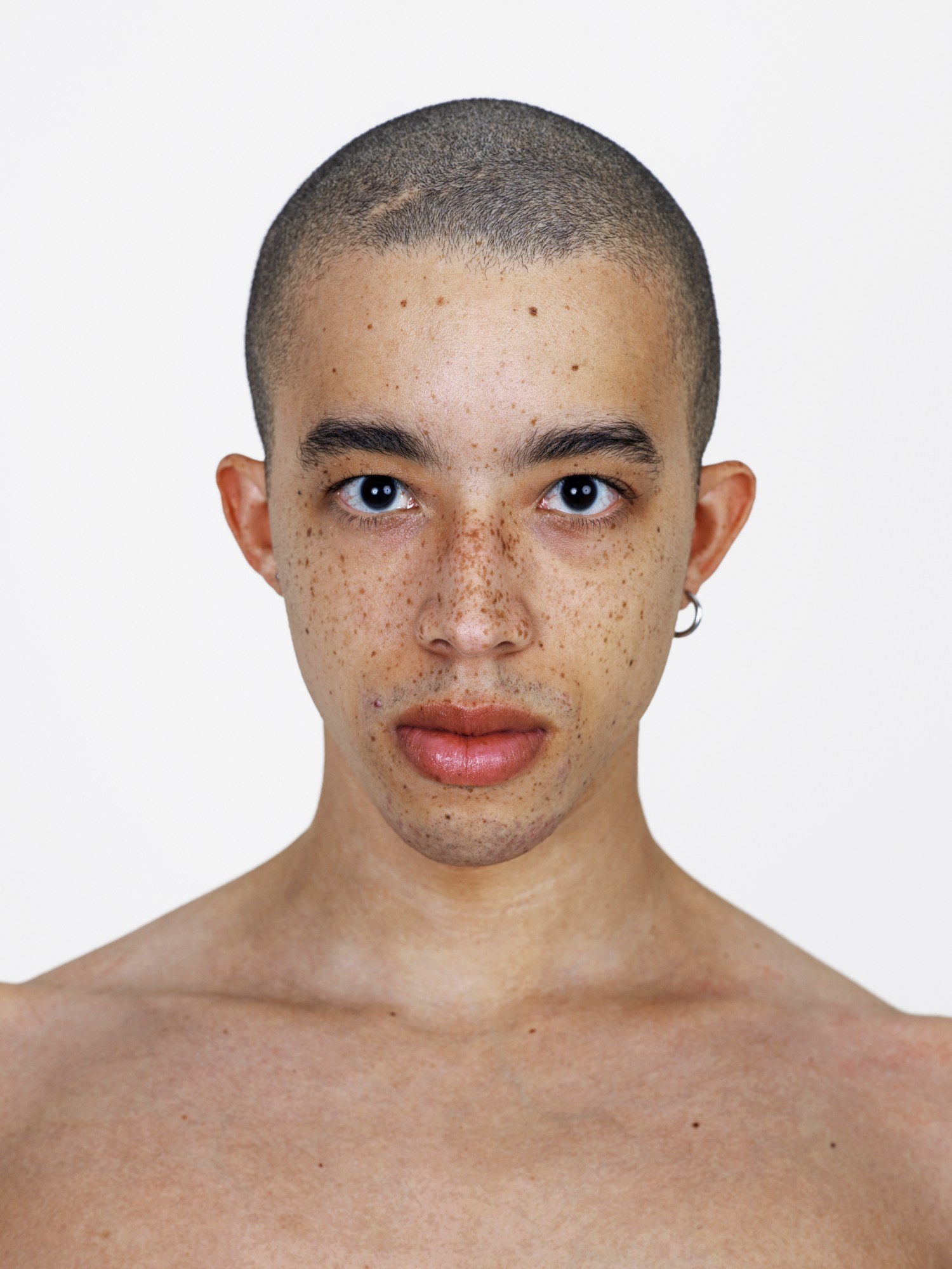 A topless man with freckles, a shaved head and one hoop earring.