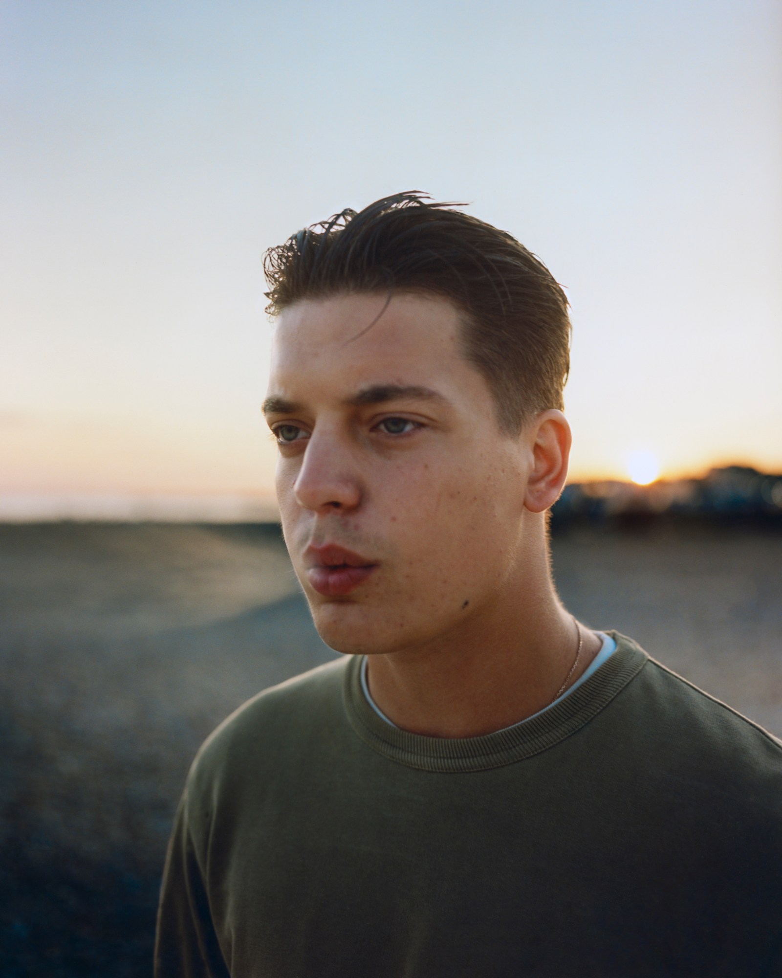 boy in green top blows out smoke on the beach.