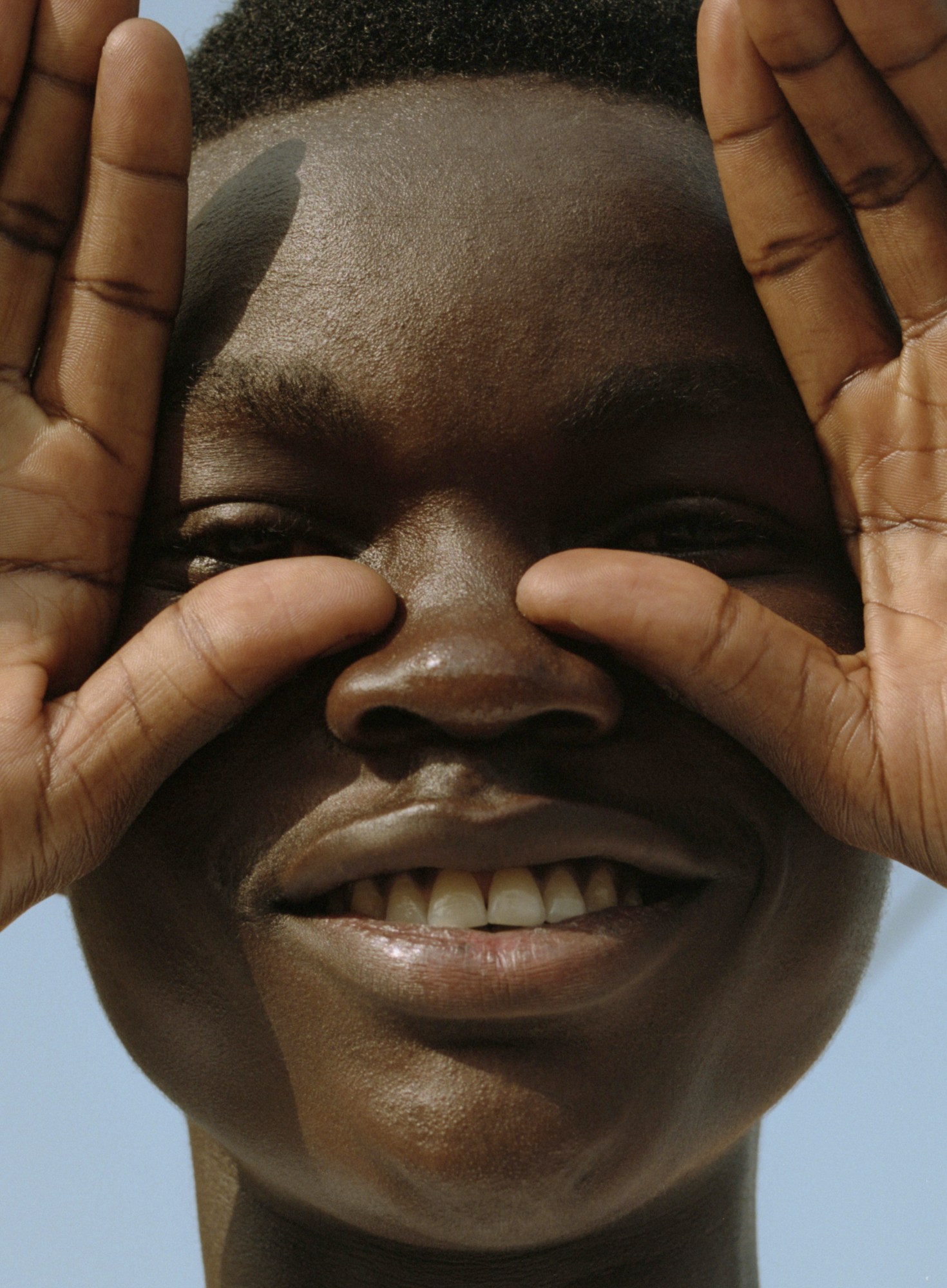 a close up of a boy looking through spaces between his fingers