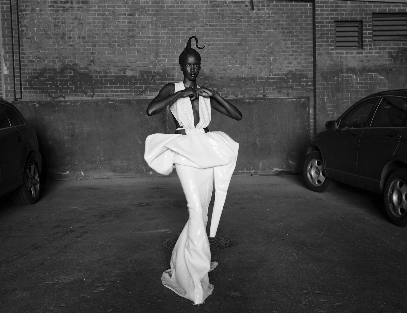 Anok Yai wears a white dress as she stands in a car park