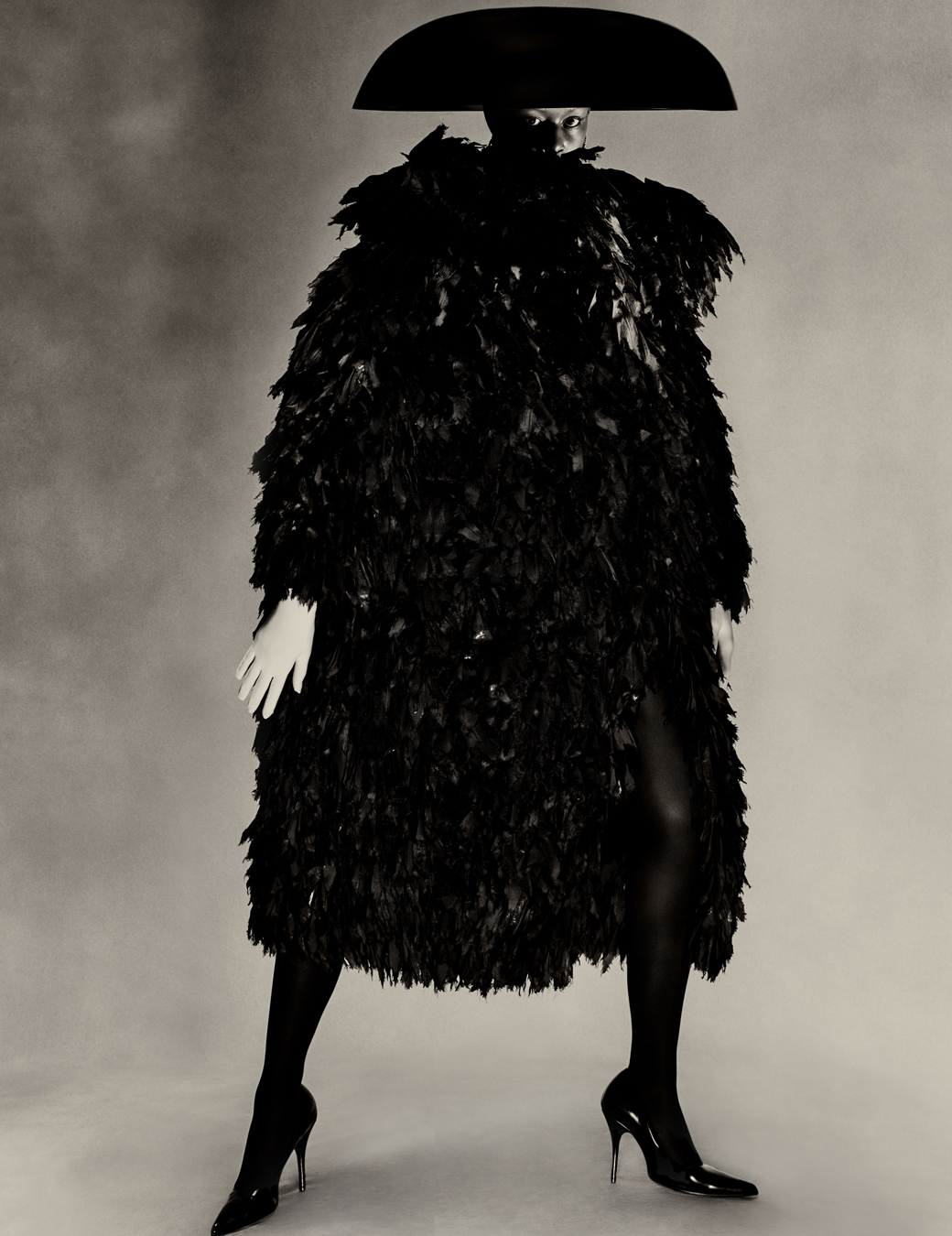 model wears an oversized black feather coat with an umbrella hat all by balenciaga.