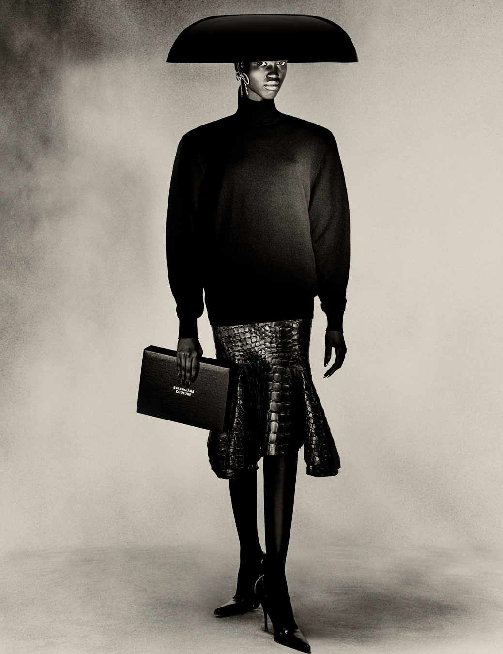 model wears skirt, turtle neck jumper, umbrella hat and bag all Balenciaga