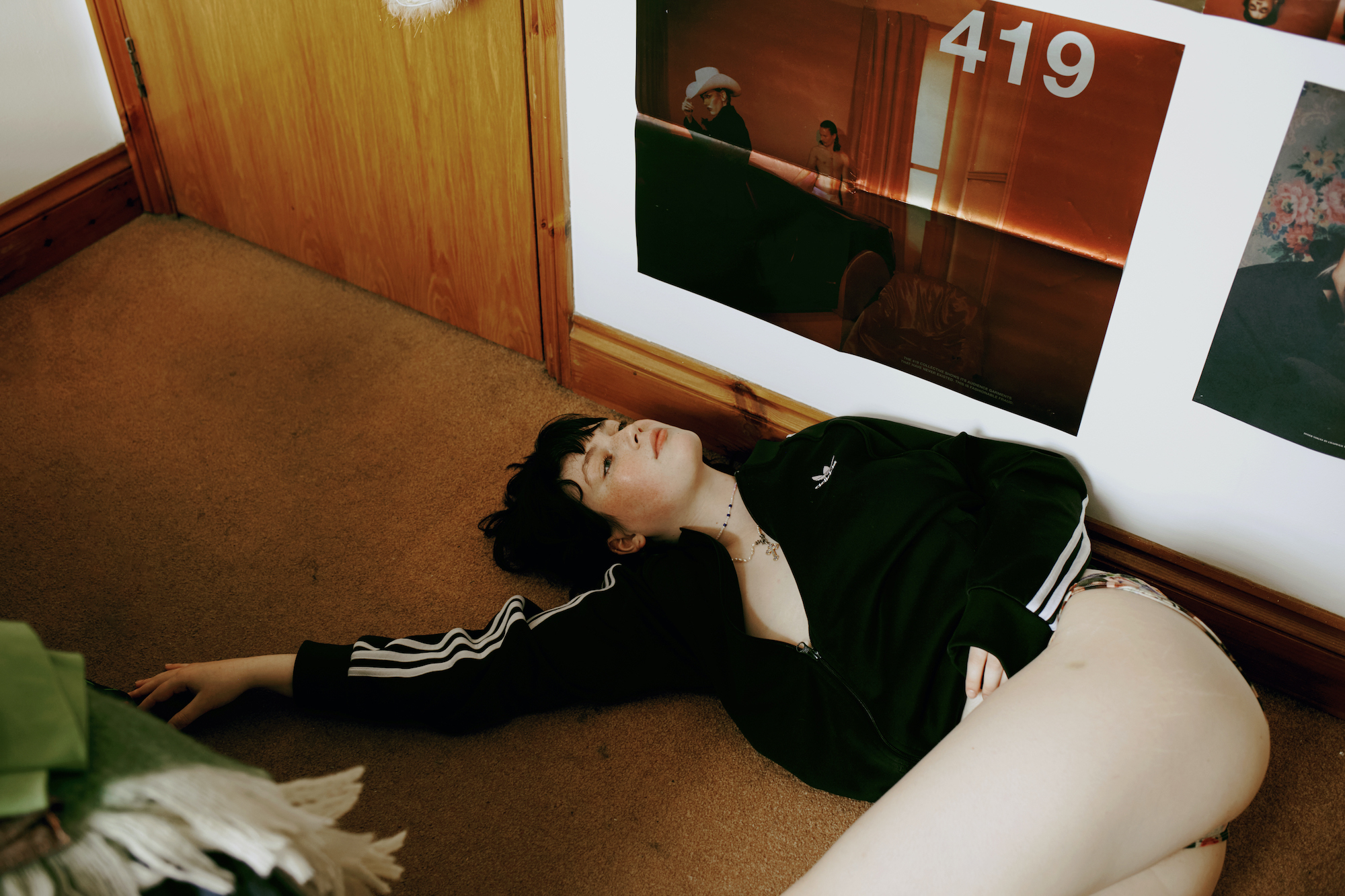 a girl in an adidas zip up top and bare legs lays on her bedroom floor looking to the ceiling