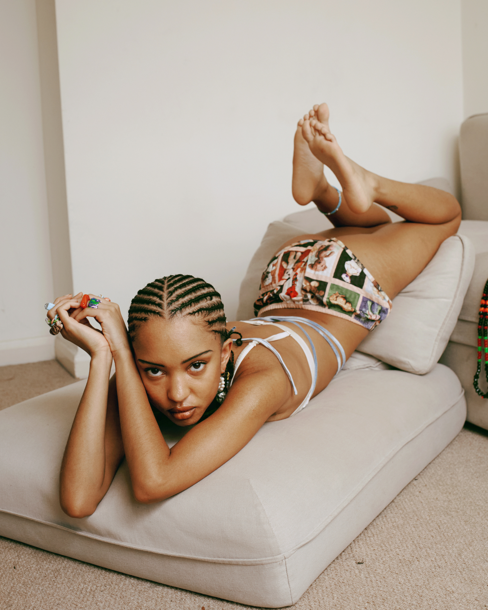 a girl with tight braids and a bikini lounges on her sofa cushions