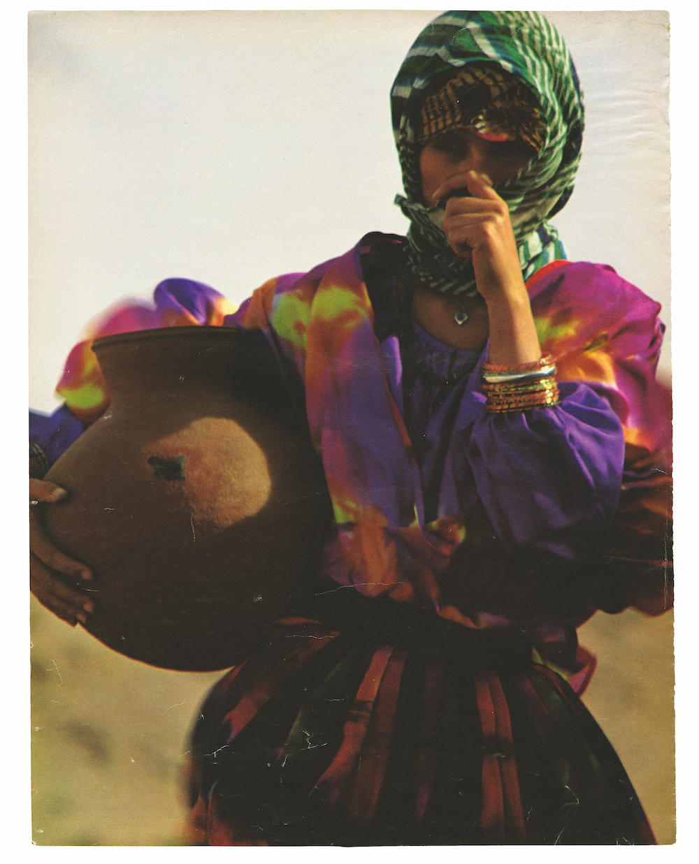 a woman in a tie-dye dress wearing a headdress and carrying a clay pot