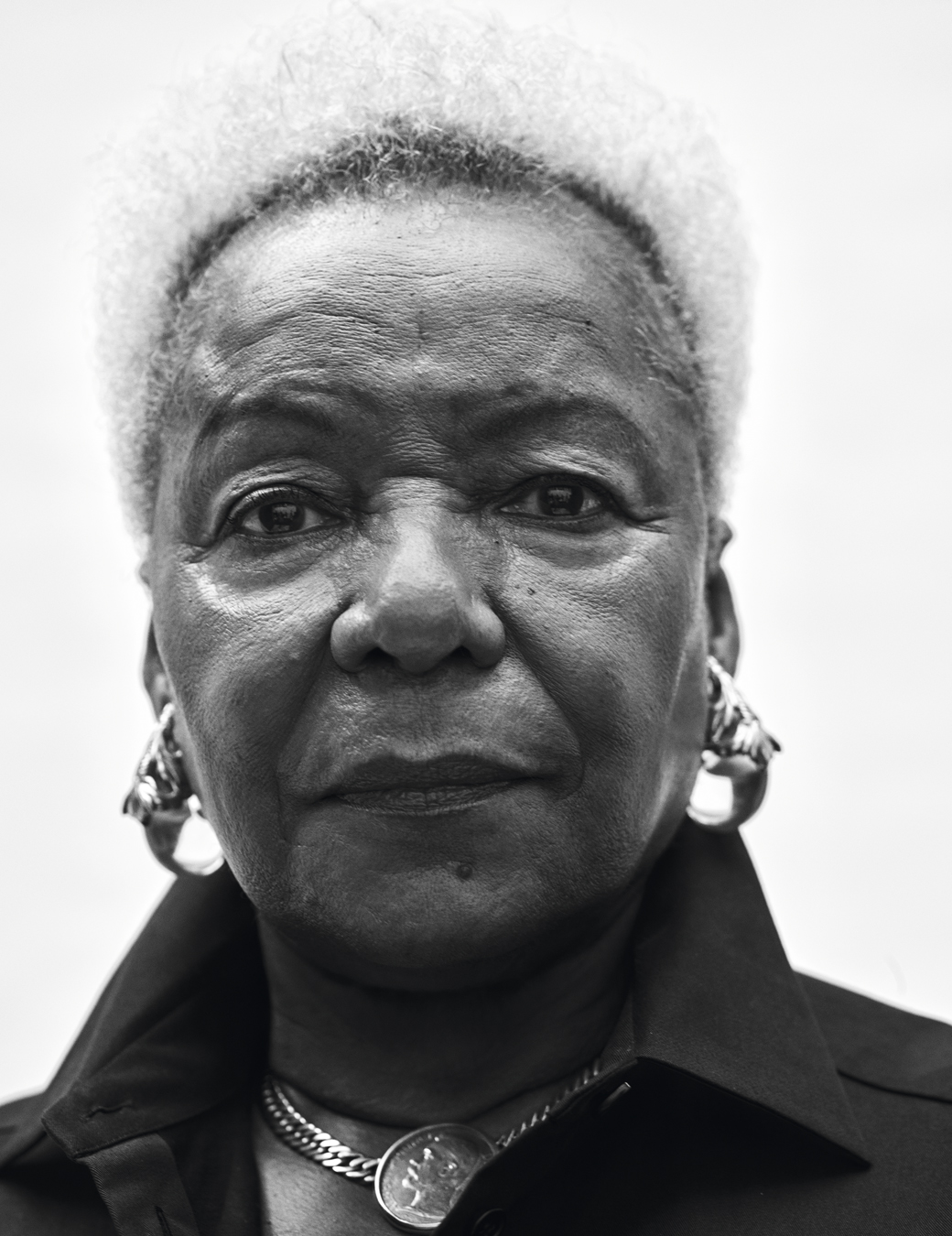 Close up of Audrey Smaltz wearing a black shirt, a chain necklace with a coin in the middle and two large metal hoop earrings.